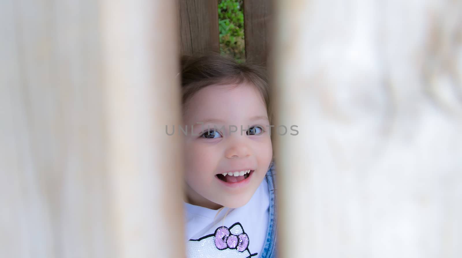 child laughs hidden behind a wooden fence