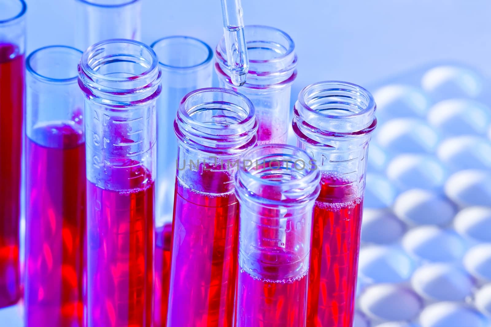 detail of pipette and test tubes with red liquid in laboratory on blue light tint background