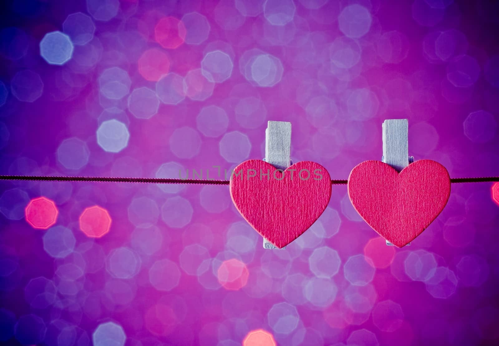 two decorative red hearts hanging against blue and violet light bokeh background, concept of valentine day by donfiore