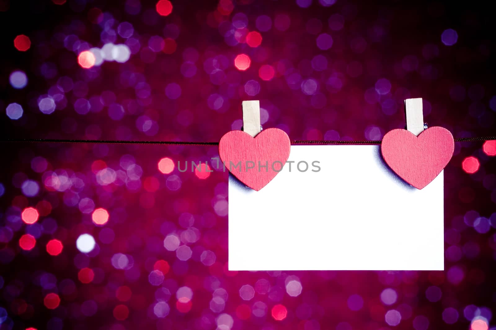 two decorative red hearts with greeting card hanging on blue and violet light bokeh background with space for text, concept of valentine day