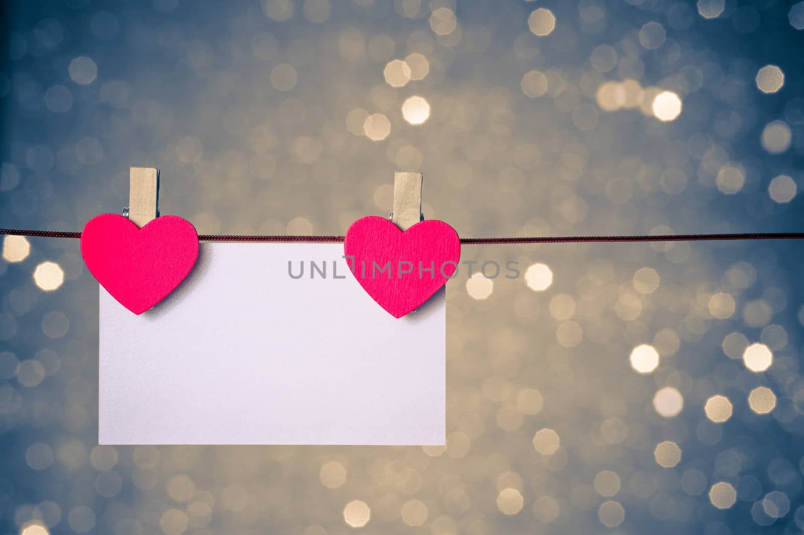 two decorative red hearts with greeting card hanging on blue and golden light bokeh background with space for text, concept of valentine day
