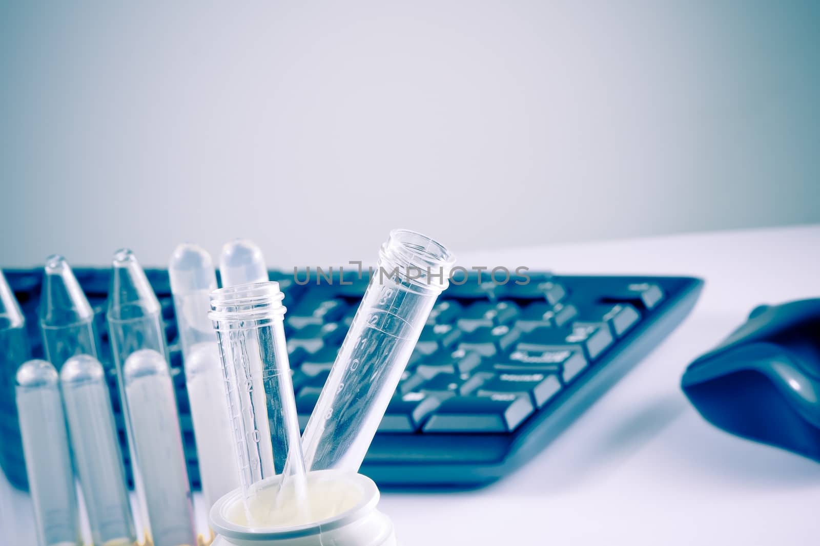 test tubes in laboratory on table near computer keyboard and mouse on table with space for text