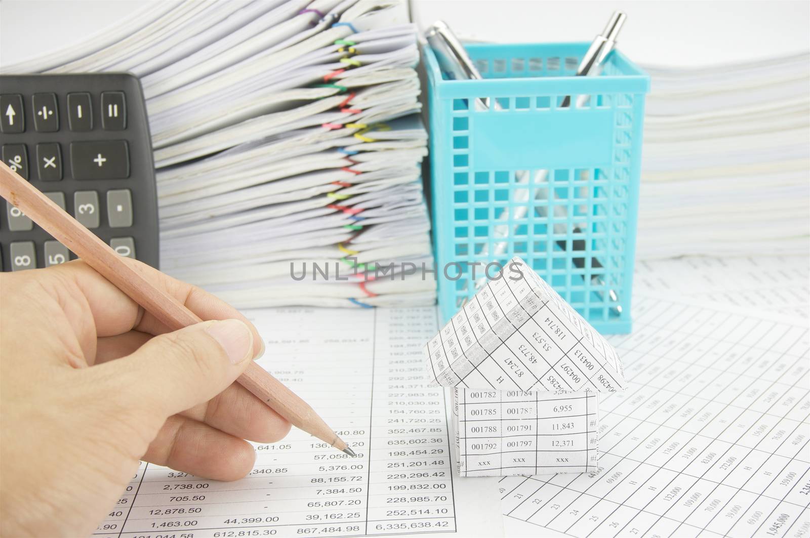 Man holding pencil for audit with house on finance account have vertical calculator and blue pen basket with paper of report and paperwork as background.