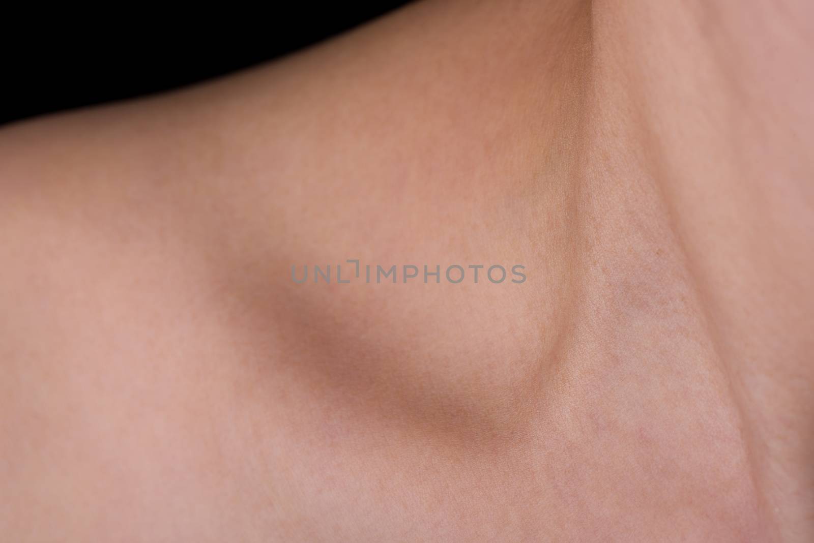 An abstract shot of a woman's neck, collarbone and shoulder with a small amount of black background showing.