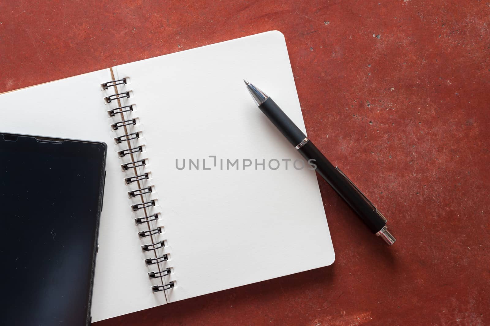 Opened notepad with pen and black smart phone on rustic cement background with low key scene.
