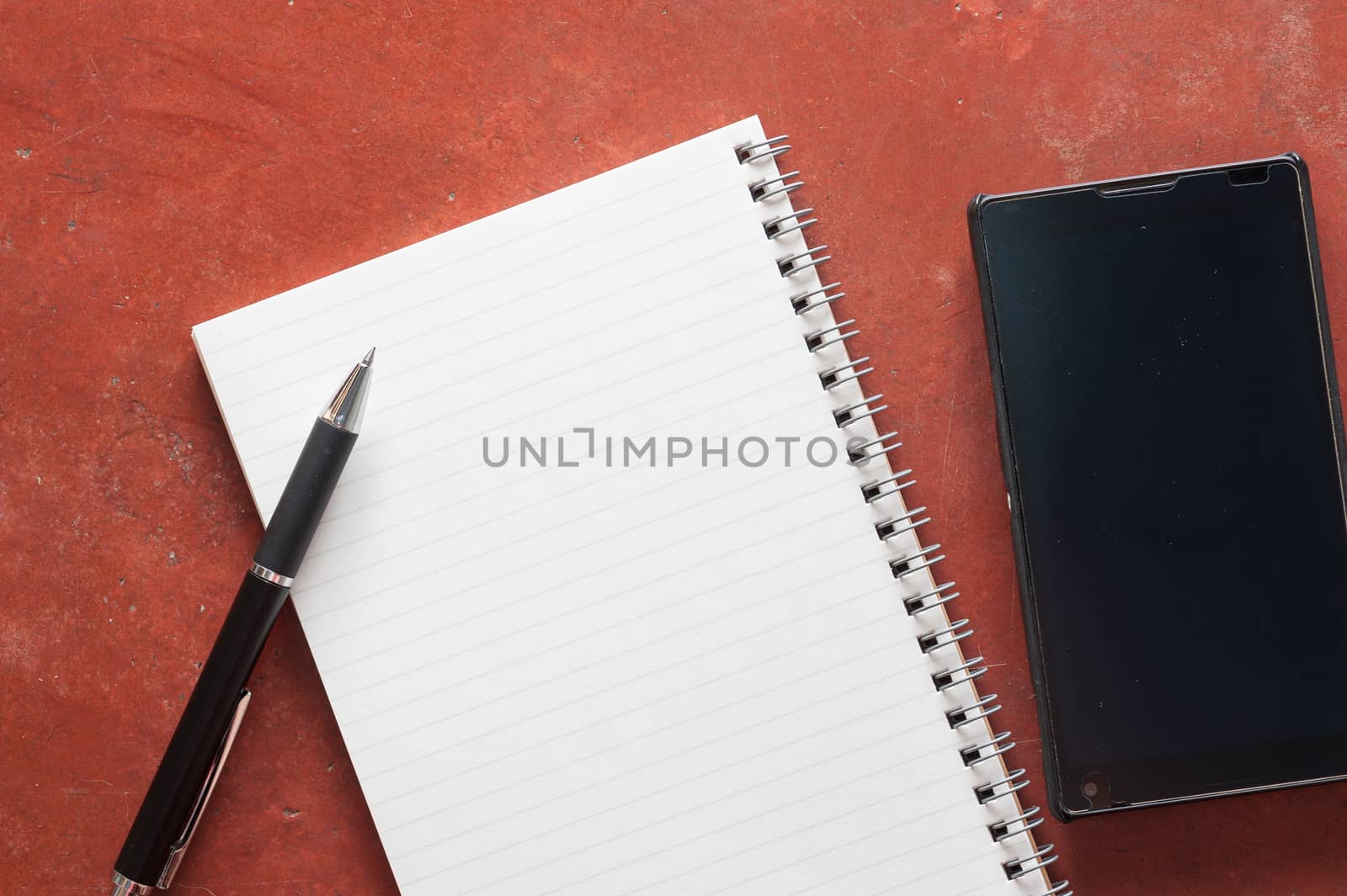 Opened notepad with pen and black smart phone on rustic cement background with low key scene.