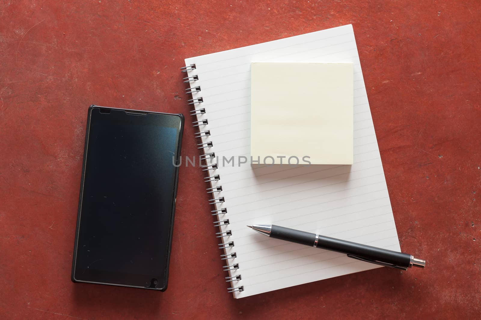 Opened notepad with pen, small sticky paper and black smart phone on rustic cement background with low key scene.