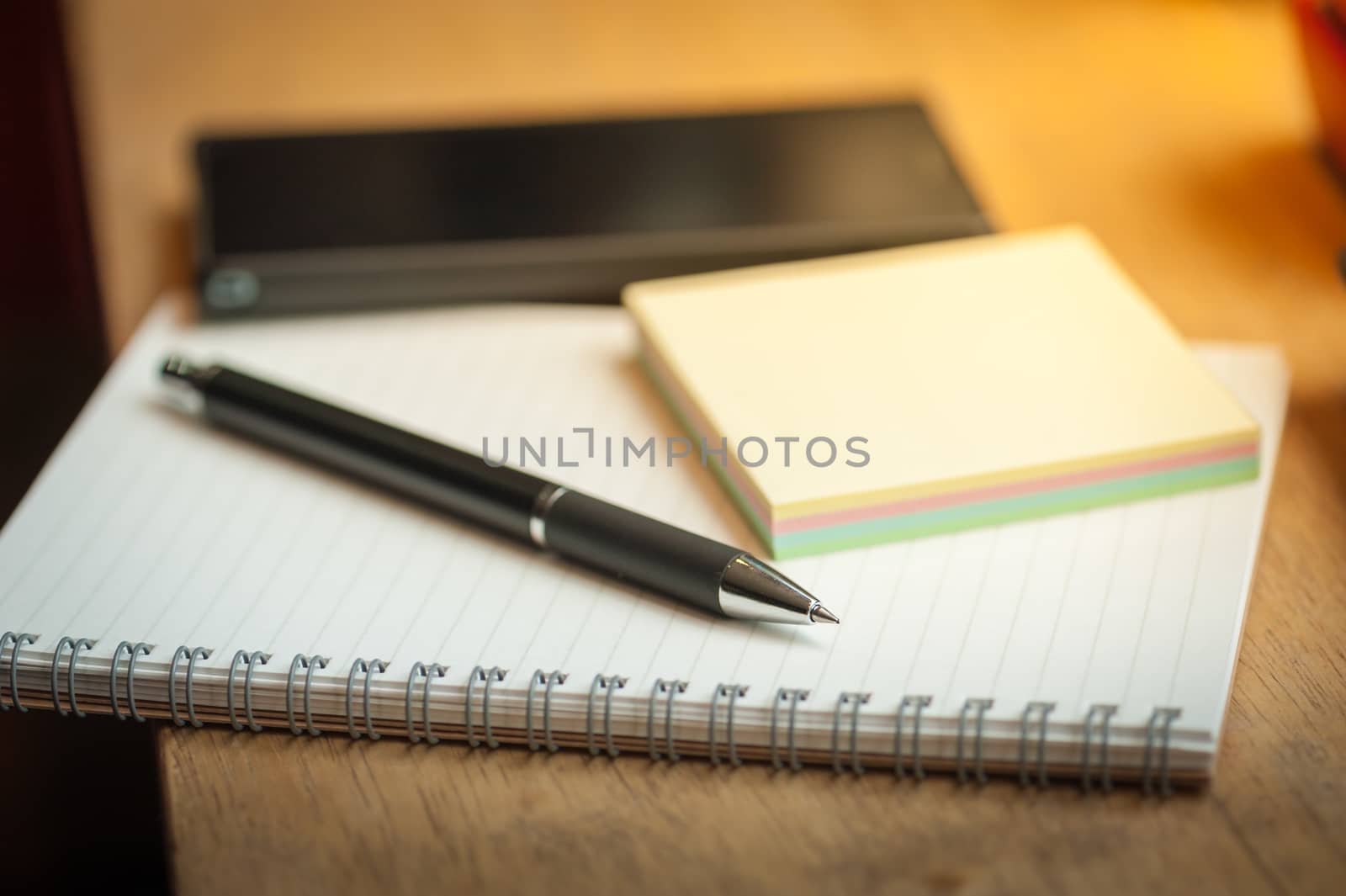 Opened notepad with pen, small sticky paper and black smart phone on wood bar in coffee shop in morning scene