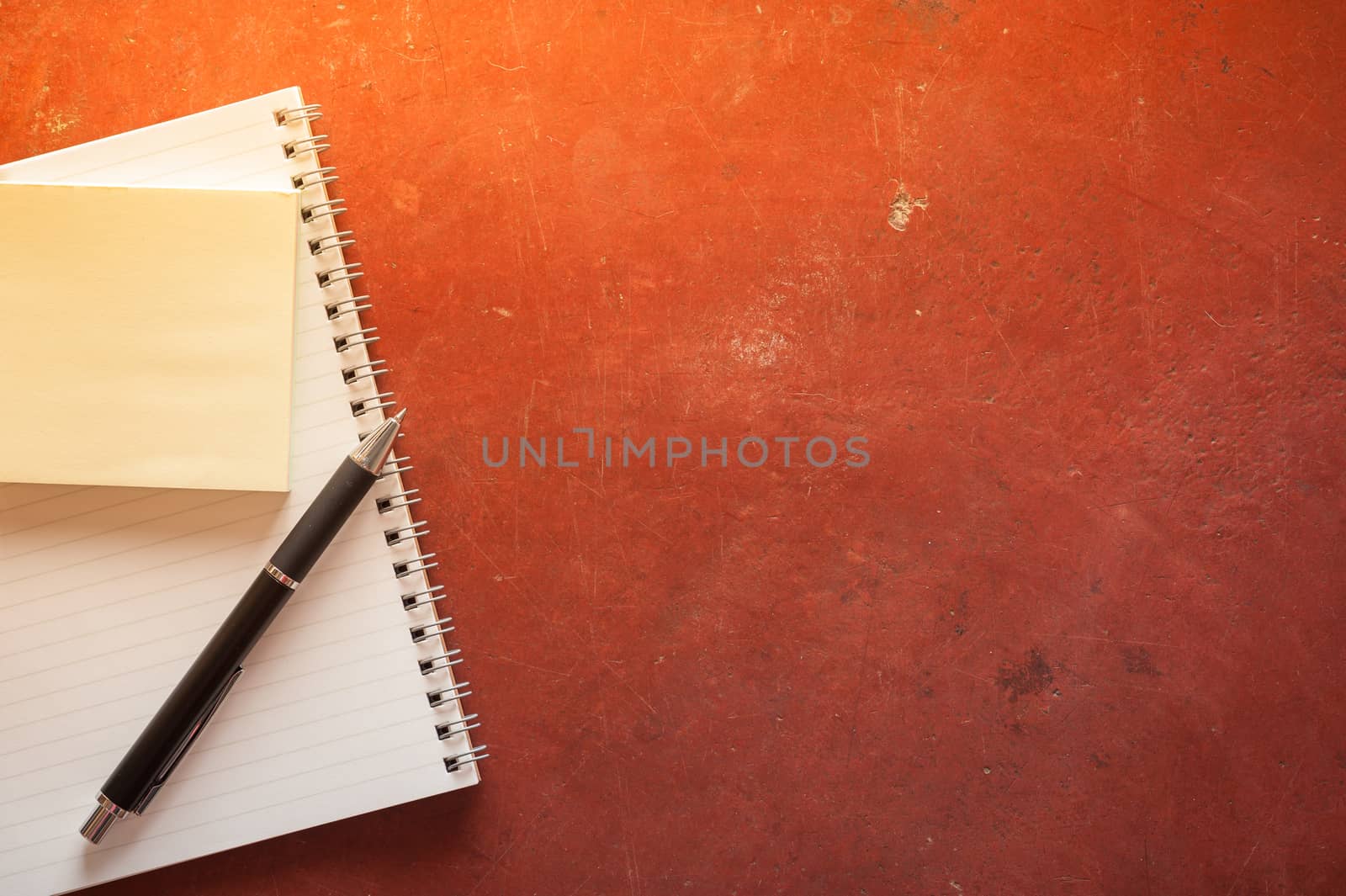 Opened notepad with pen, small sticky paper on red cement background with morning scene