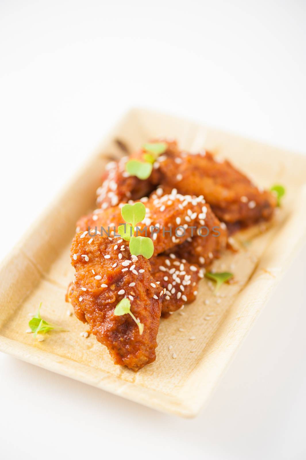 Korean fusion style deep fried chicken wings seasoned with Korean spicy kimchi sauce on square ceramic dish