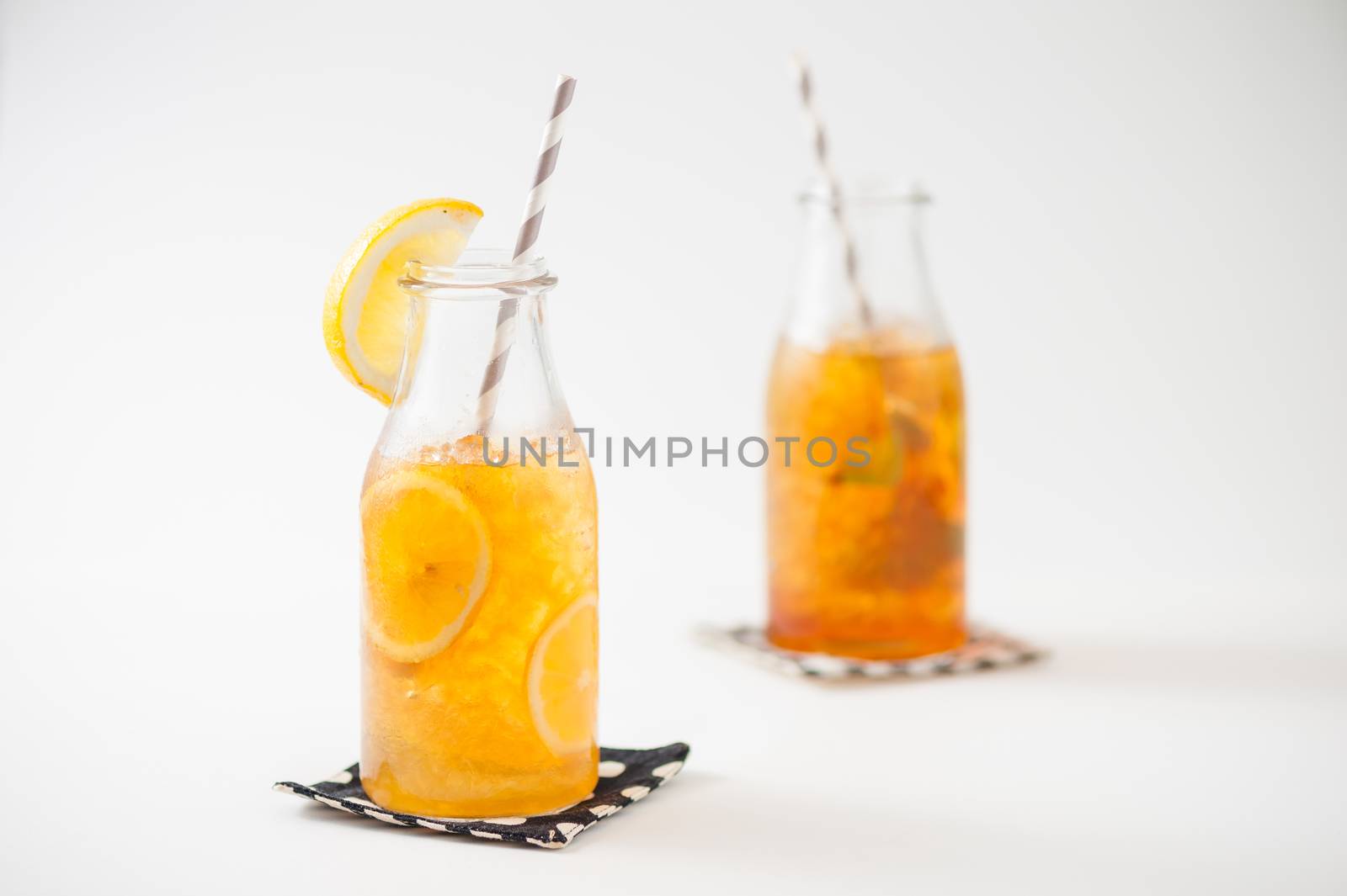 Iced lemon tea garnished with lemon in glass bottle with peppermint toffee tea on background