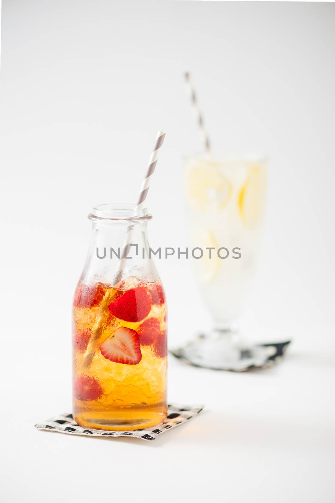 Iced strawberry tea in glass bottle with striped straw with iced lemonade in background