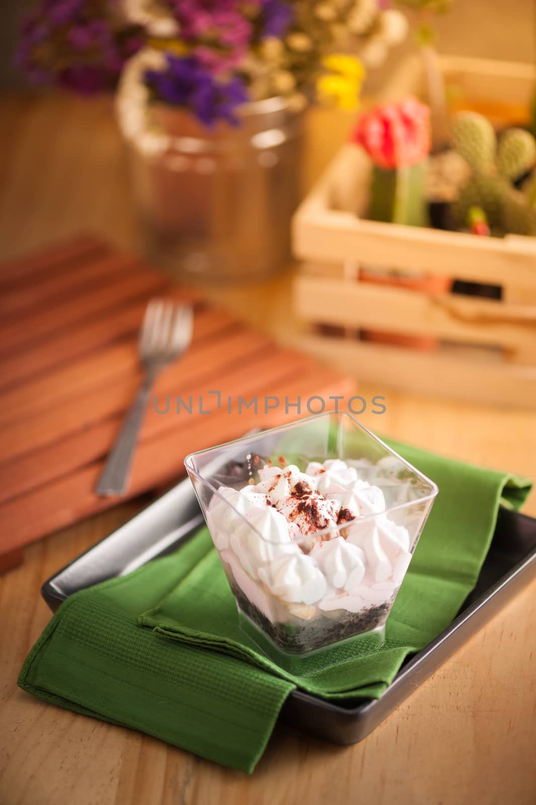 Banoffee pie in plastic cup on green napkin in black dish on wood table with afternoon scene