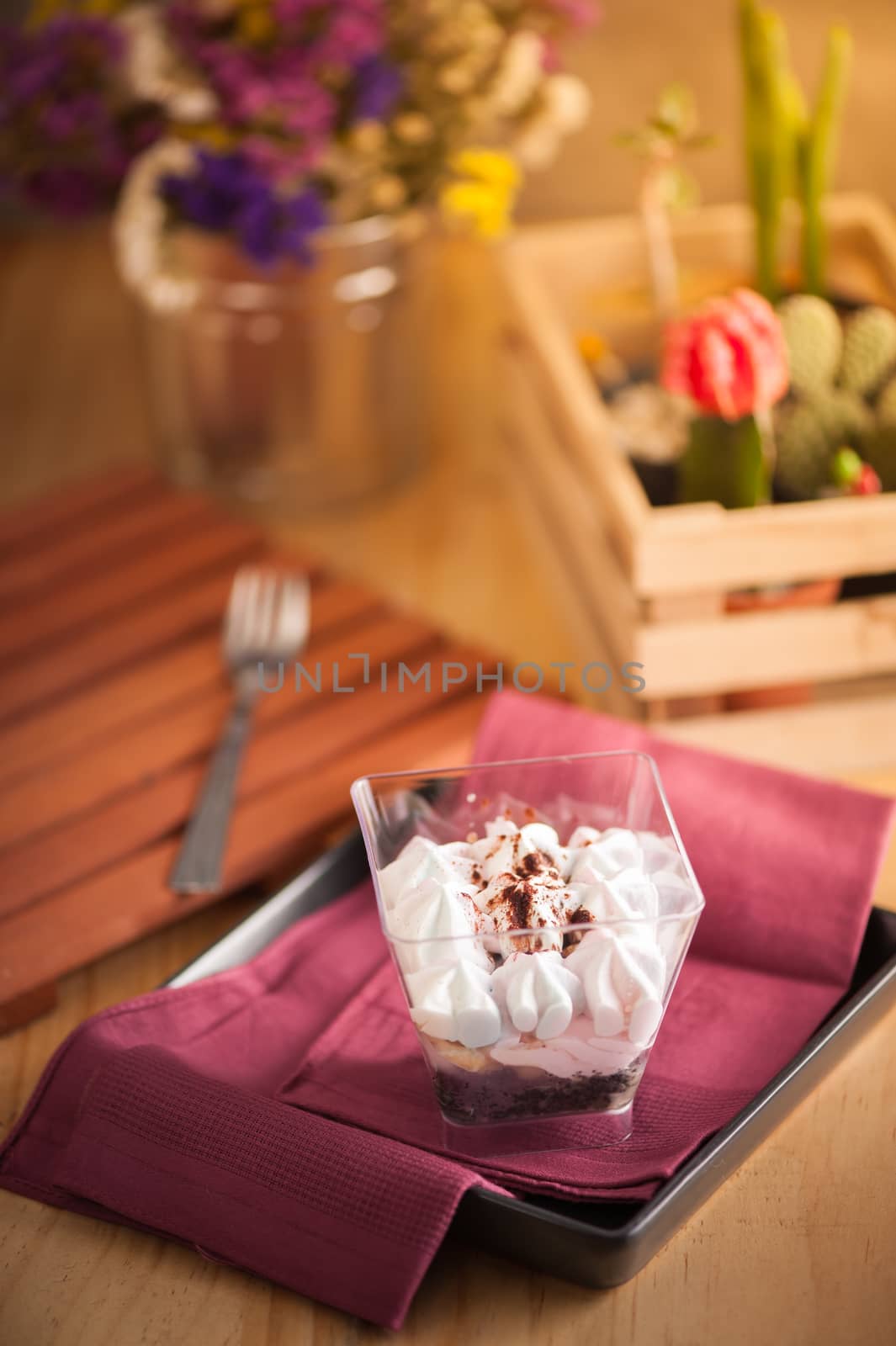 Banoffee pie in plastic cup on red napkin in black dish on wood table with afternoon scene
