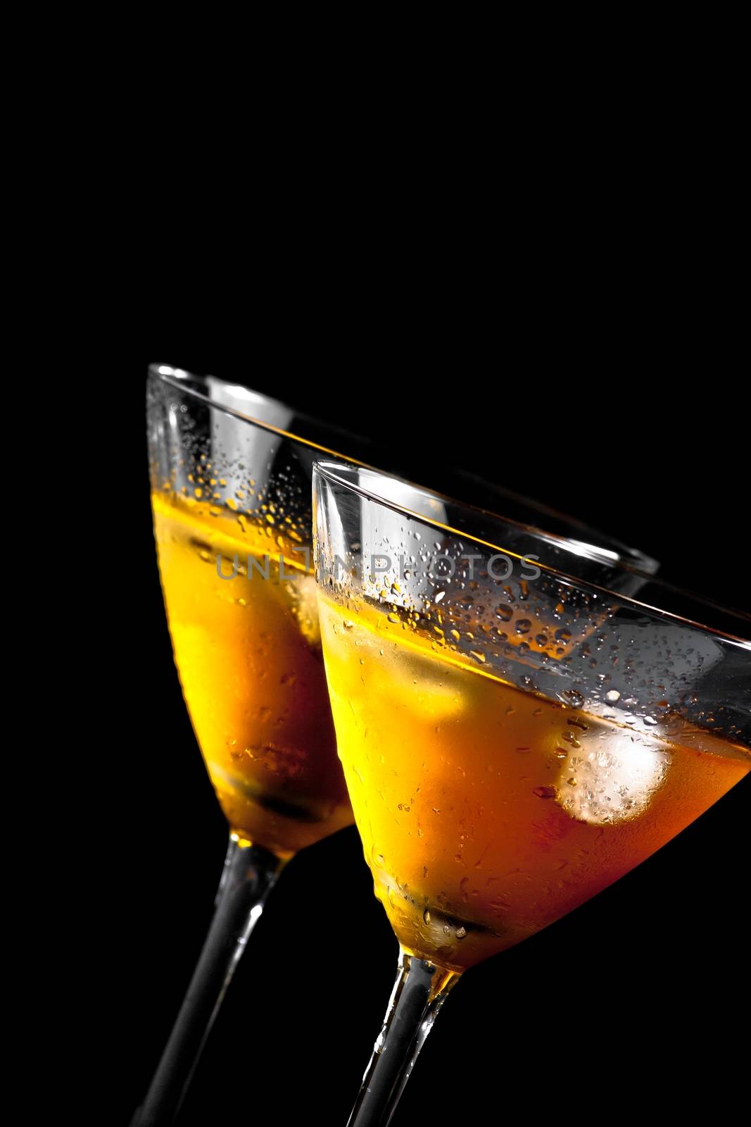 two glasses tilted of fresh cocktail with ice on black background with space for text