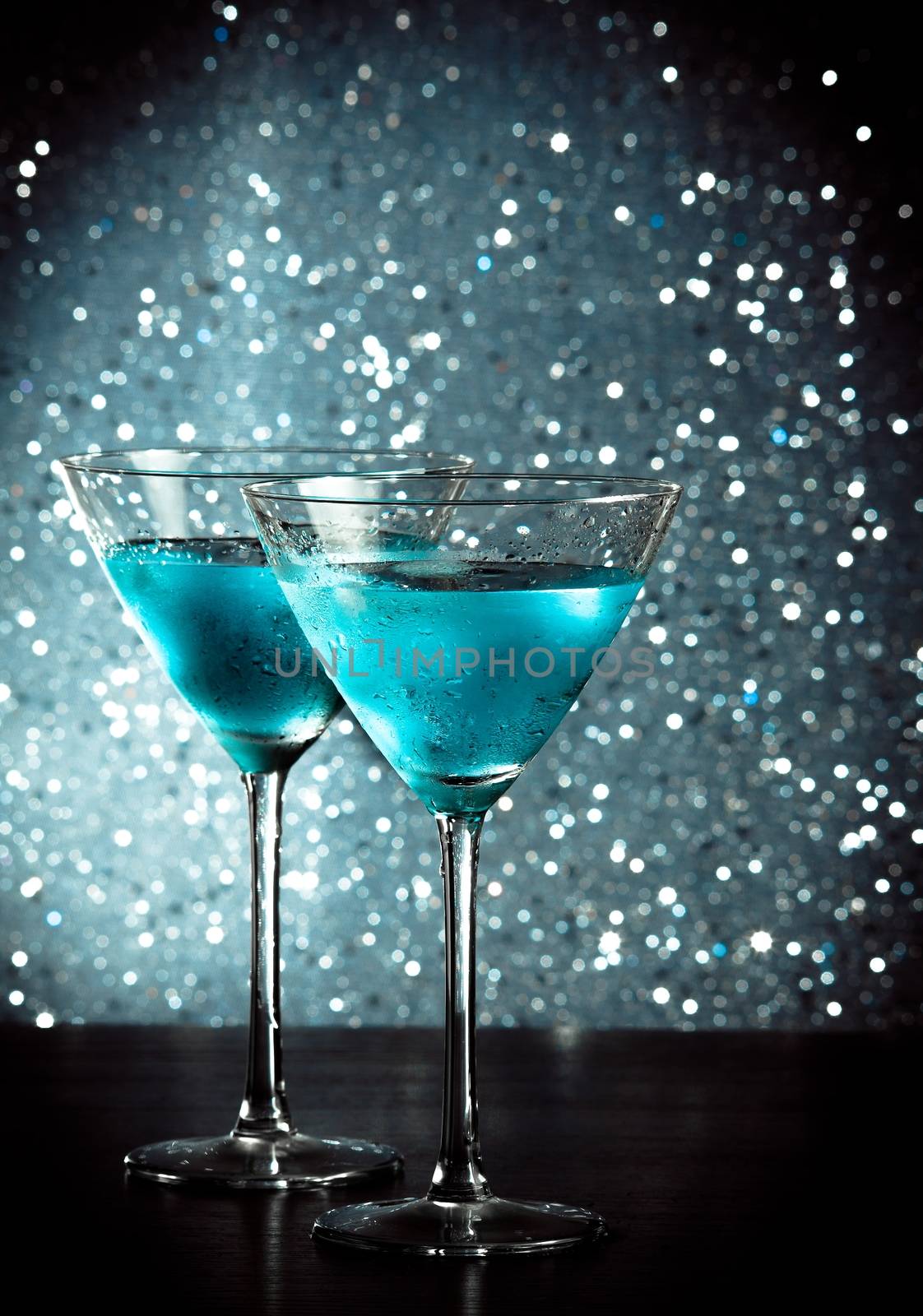 glasses of fresh blue cocktail with ice on blue tint light bokeh background on bar table