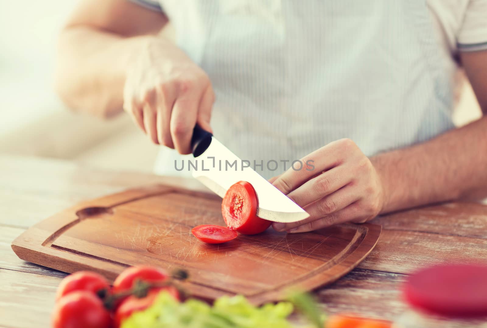 male hand cutting tomato on board with knife by dolgachov