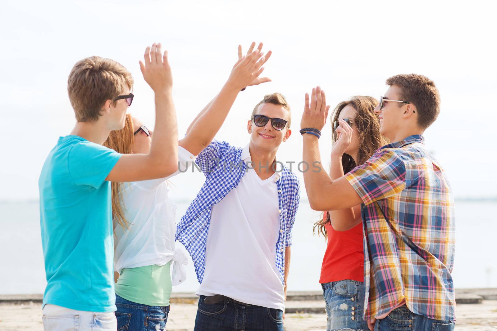 friendship, leisure, summer, gesture and people concept - group of smiling friends making high five outdoors