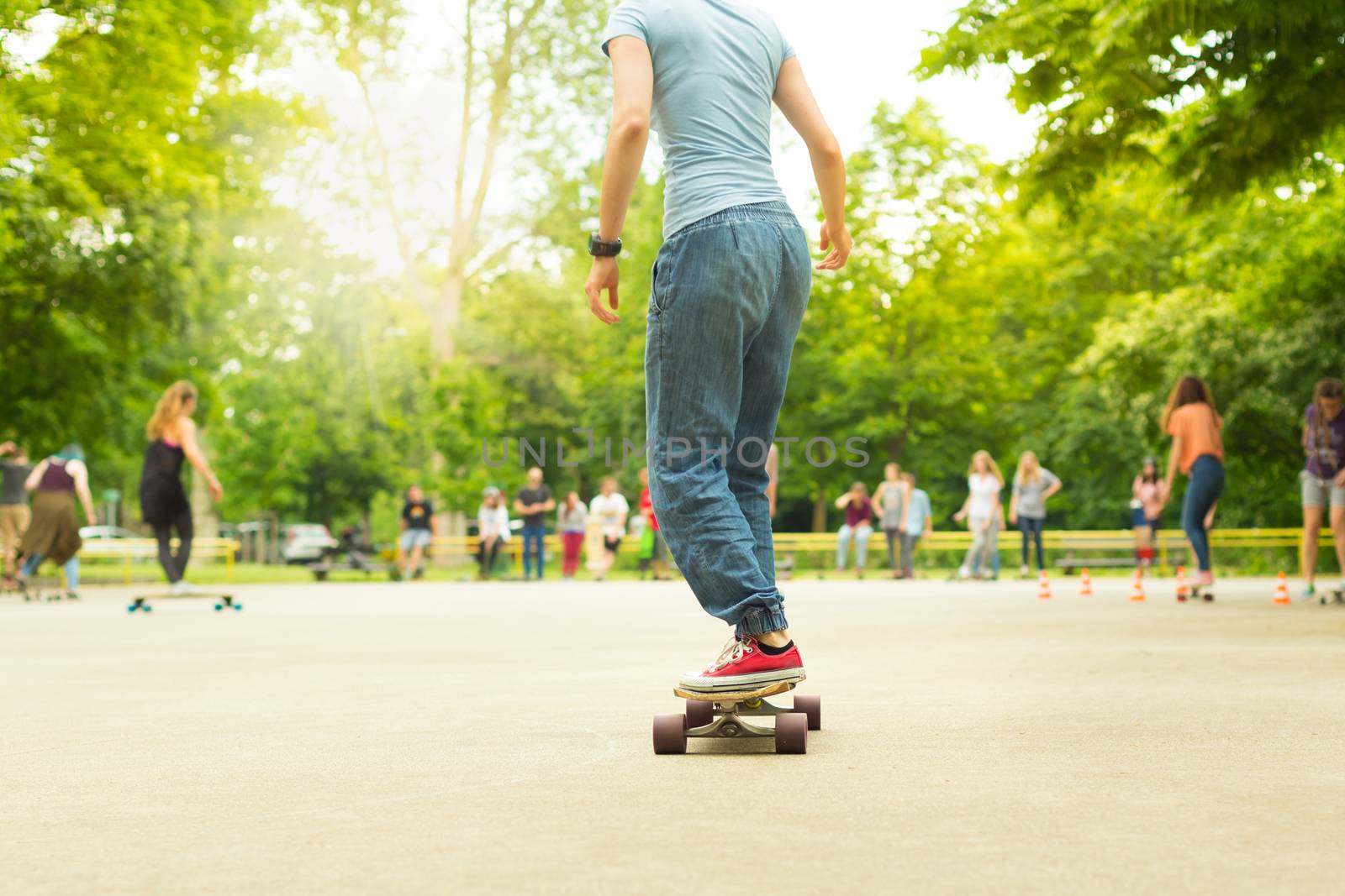 Teenage girl wearing blue jeans and sneakers practicing long board riding in skateboarding park. Active urban life. Urban subculture.