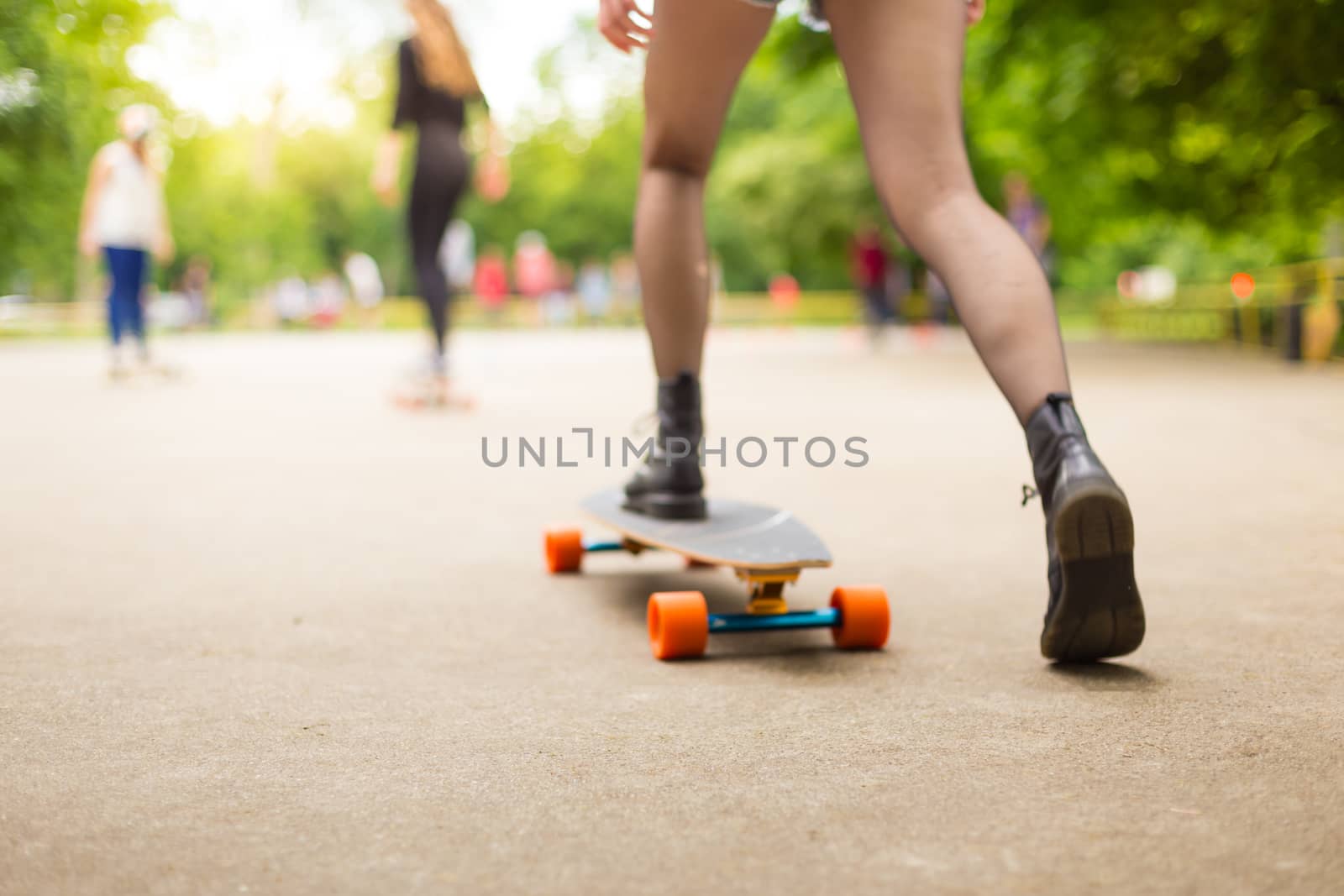 Teenage girl wearing black boots and stockings practicing long board riding outdoors in skateboarding park. Active urban life. Urban subculture. Motion blured. Focus on the floor for copy space.