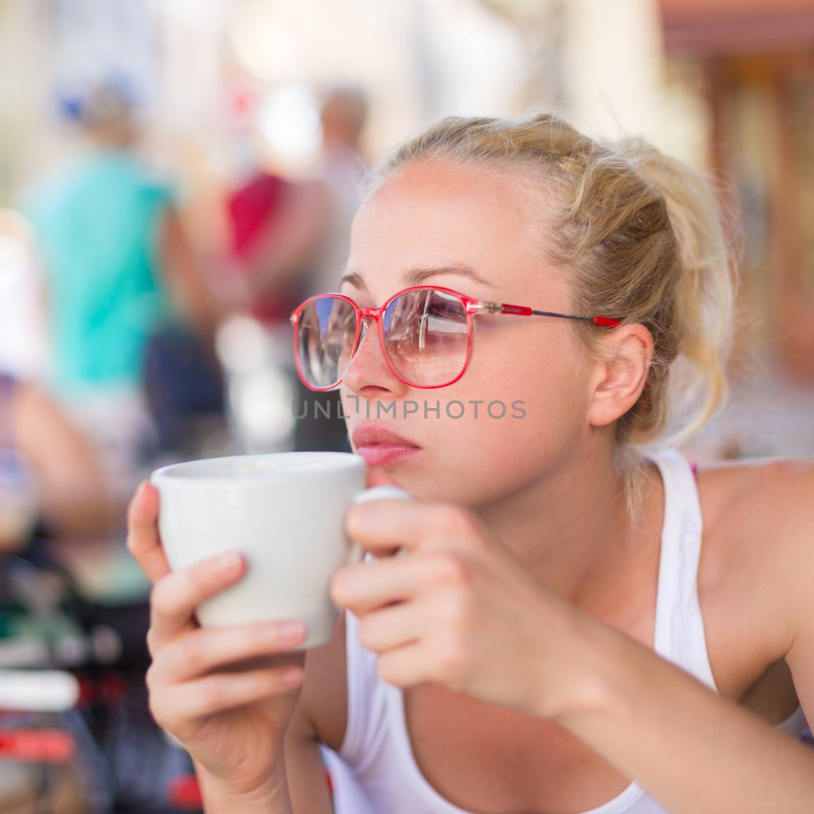 Calm casual blond lady enjoying cup of coffee outdoor in typical italian  street coffee house on warm summer day.