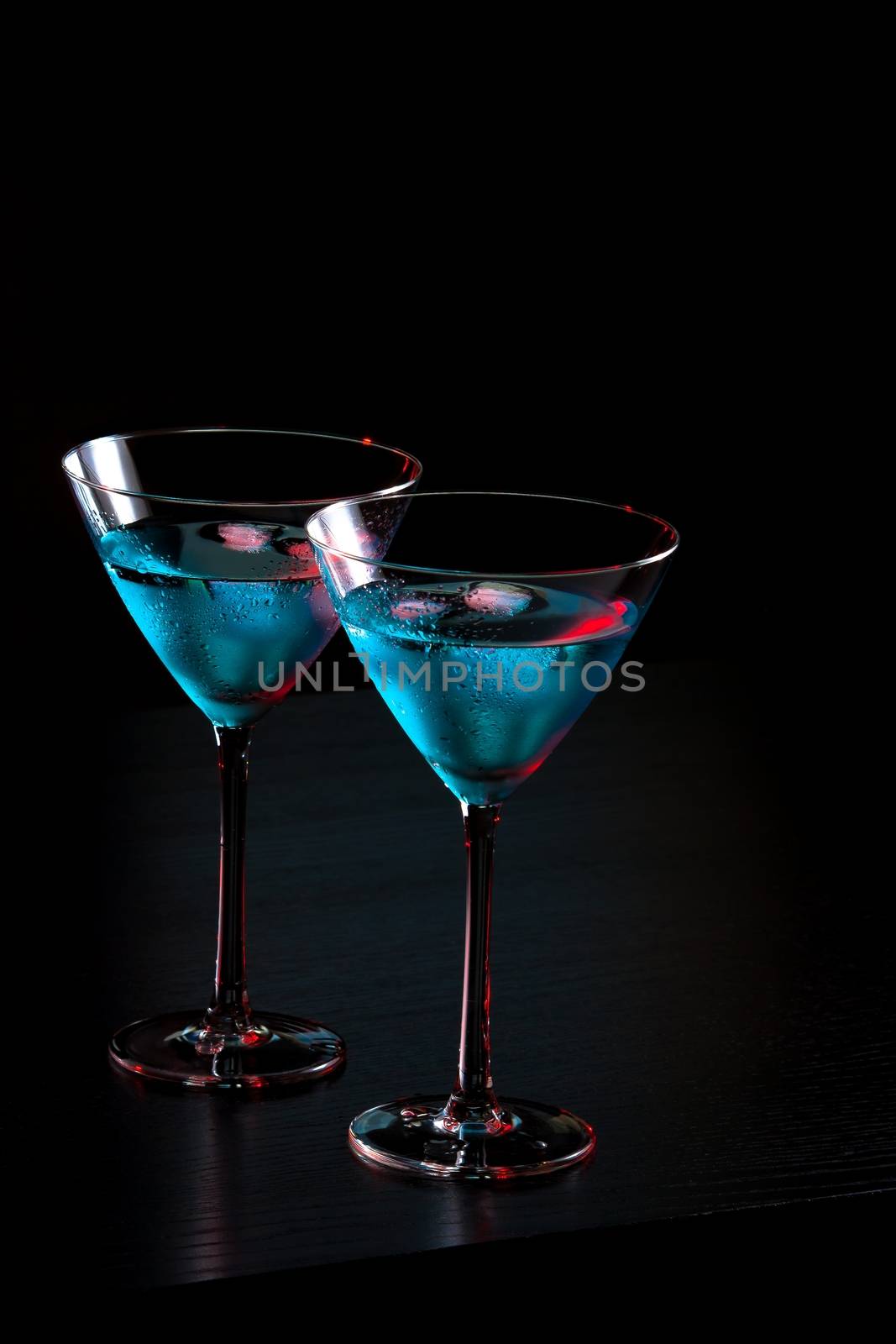 glasses of fresh blue cocktail with ice on red tint light and black background on bar table with space for text