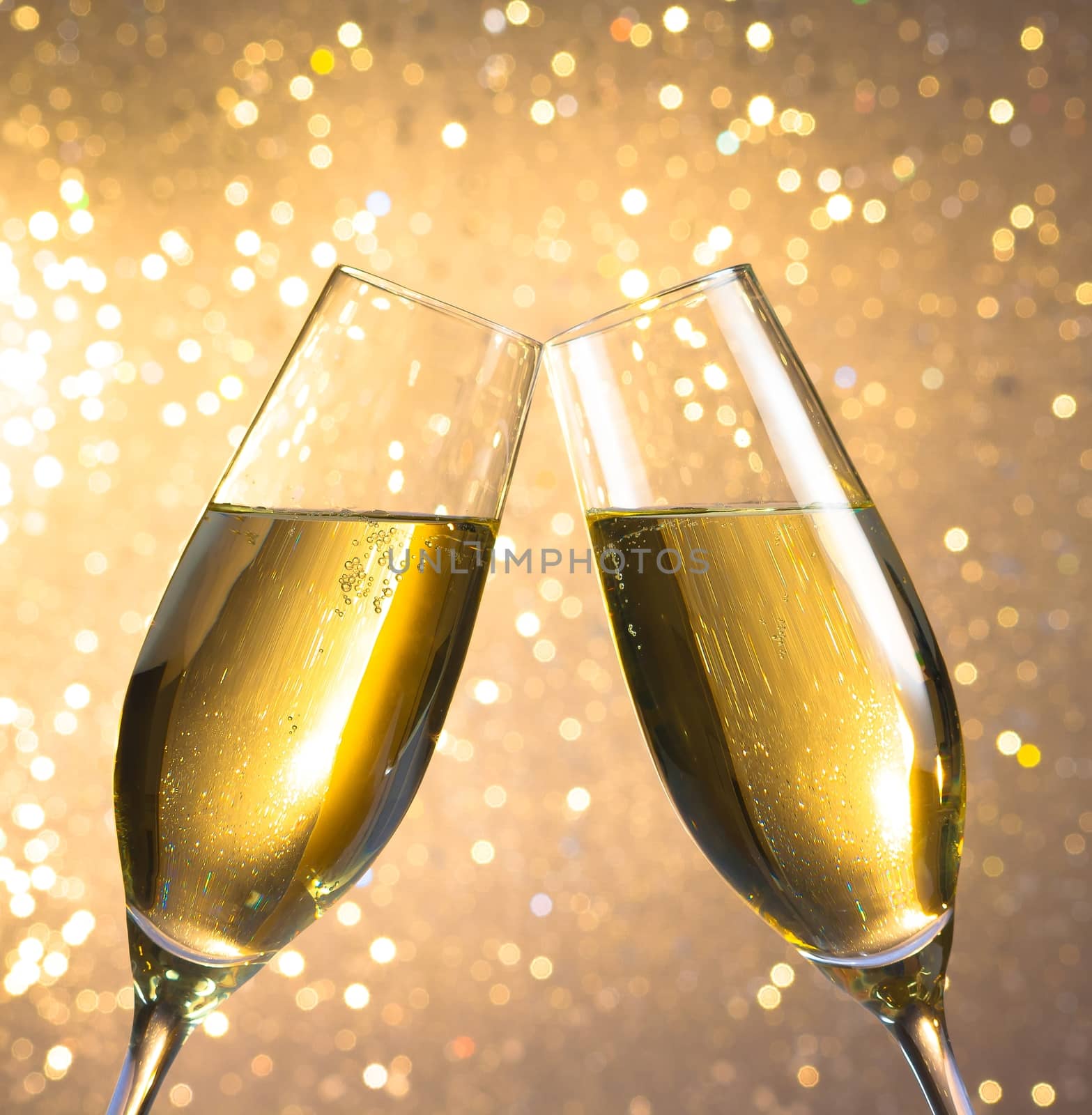 pair of a champagne flutes with golden bubbles on light bokeh background by donfiore