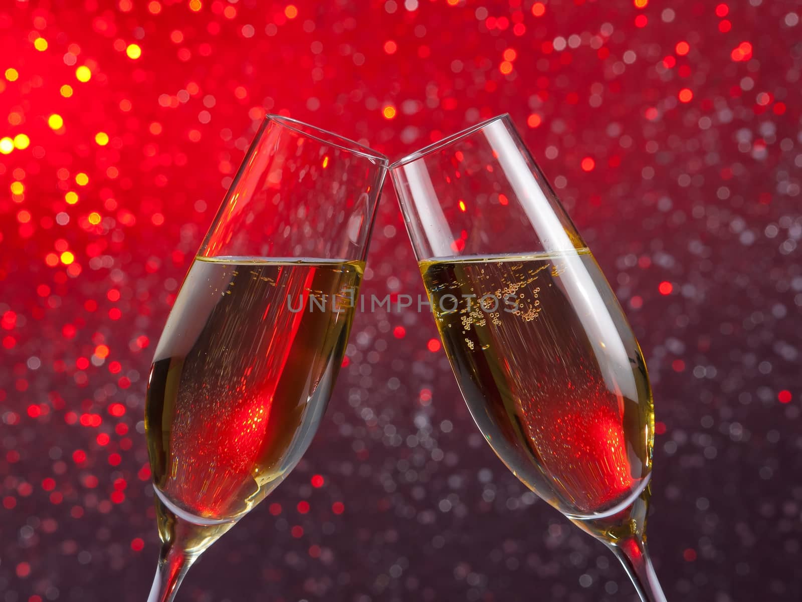pair of a champagne flutes with gold bubbles on red and violet light bokeh background by donfiore