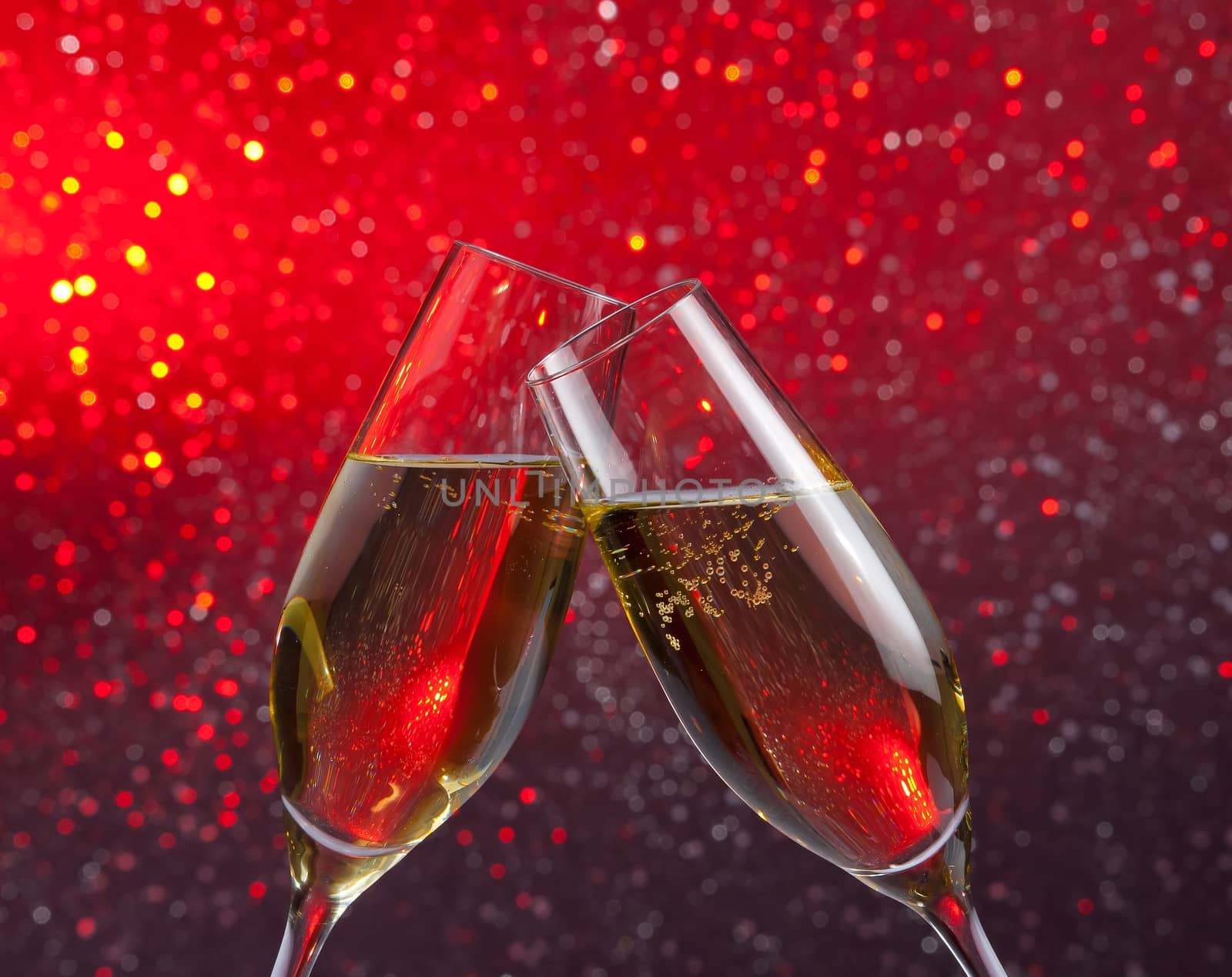 pair of a champagne flutes with gold bubbles make cheers on red and violet light bokeh background