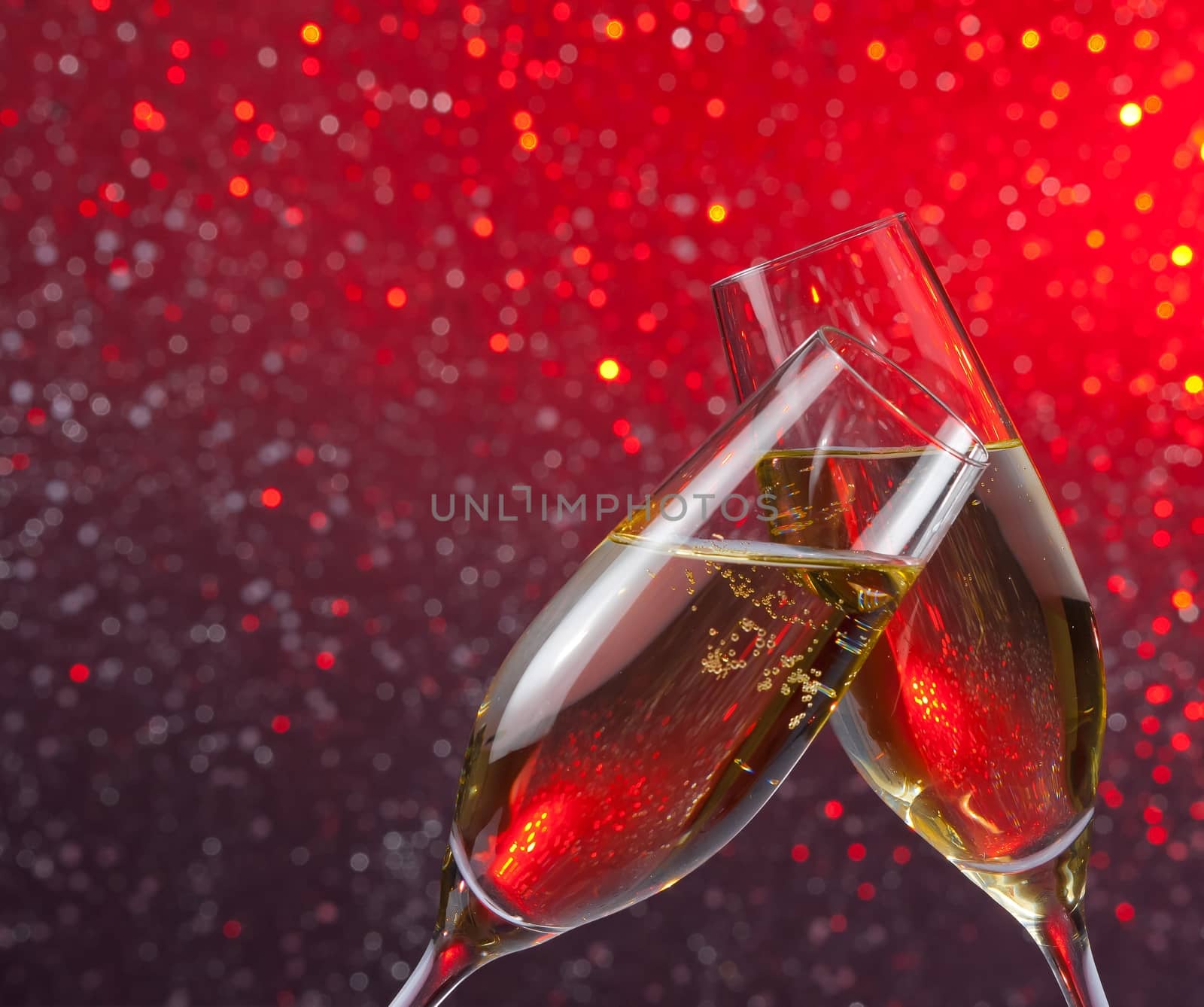 pair of champagne flutes with gold bubbles make cheers on red and violet light bokeh background with space for text