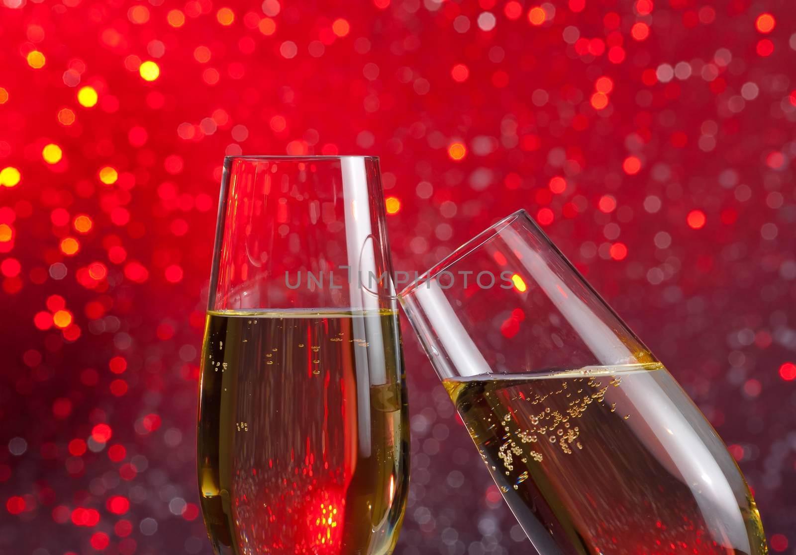 two champagne flutes with gold bubbles make cheers on red light bokeh background with space for text