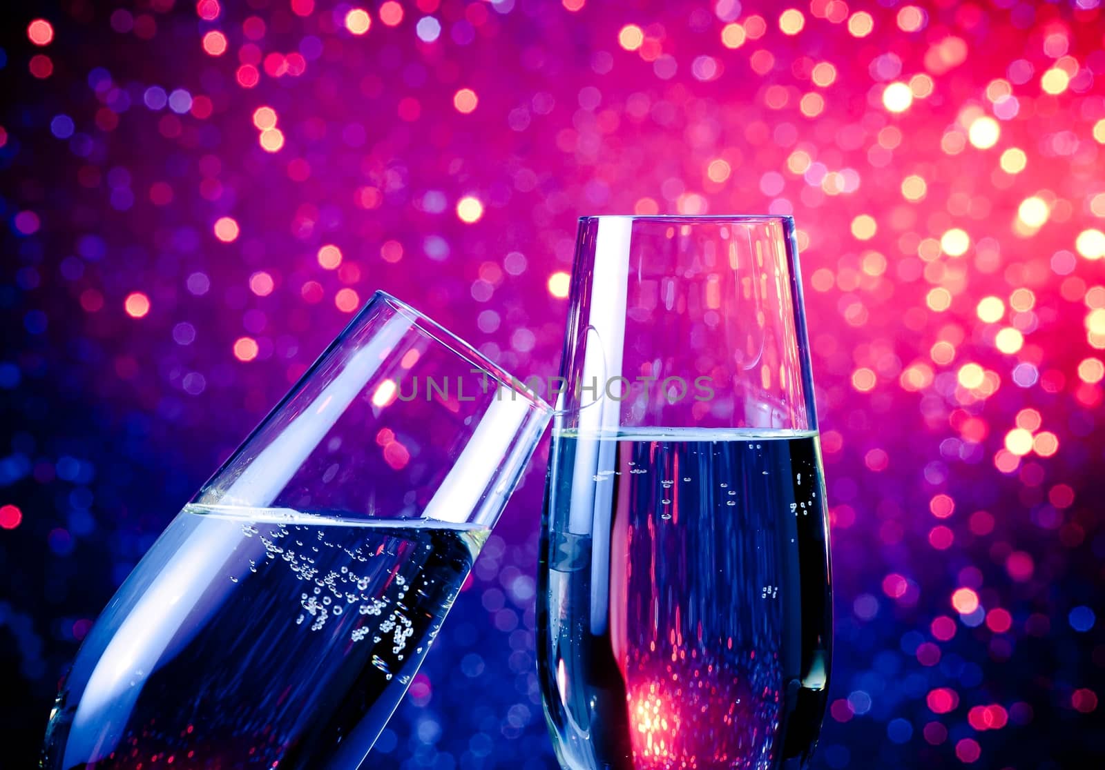 two champagne flutes with gold bubbles on blue tint light bokeh background by donfiore