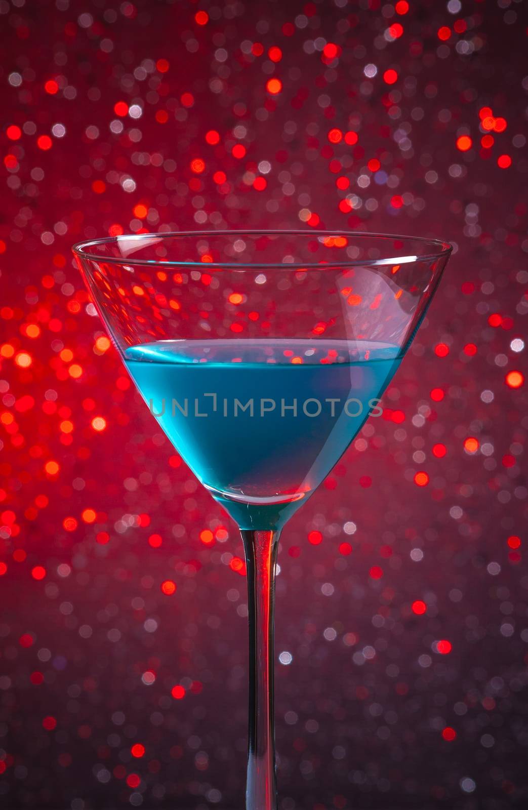 one glass blue cocktail on red tint light bokeh background