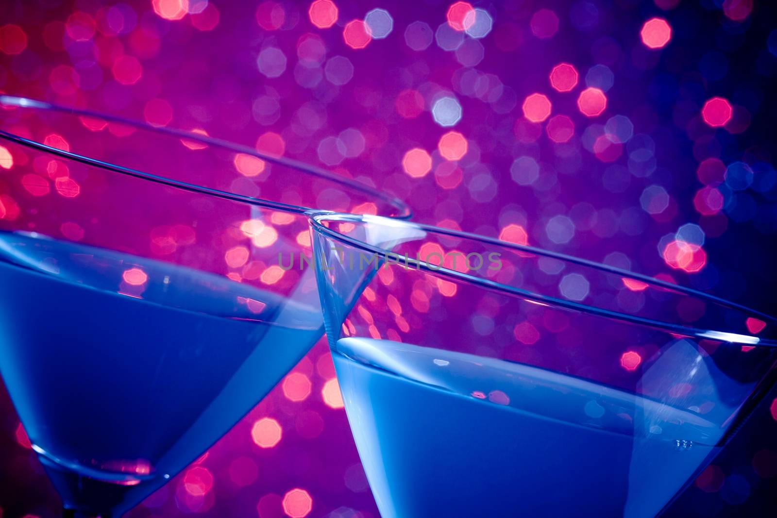 detail of a pair of glasses of blue cocktail on blue and violet tint light bokeh background