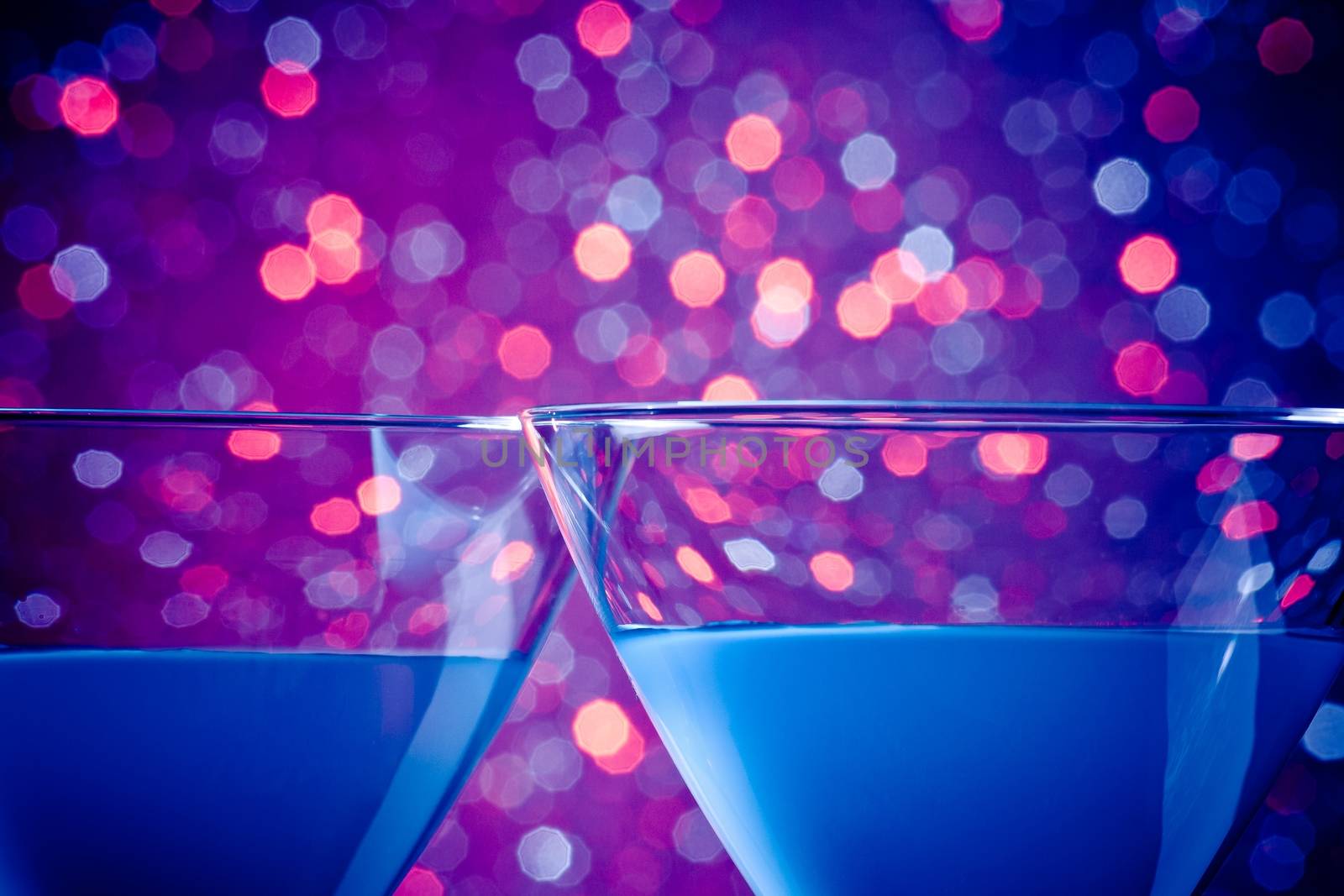 detail of a pair of glasses of blue cocktail on blue and violet tint light bokeh background with space for text