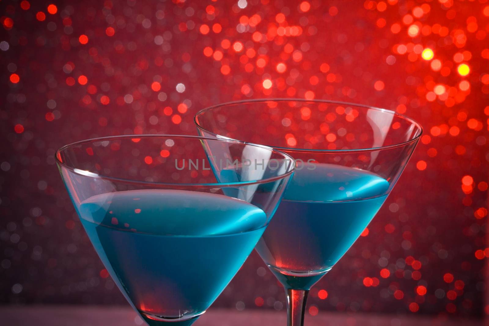 detail of a pair of glasses of blue cocktail on red tint light bokeh background