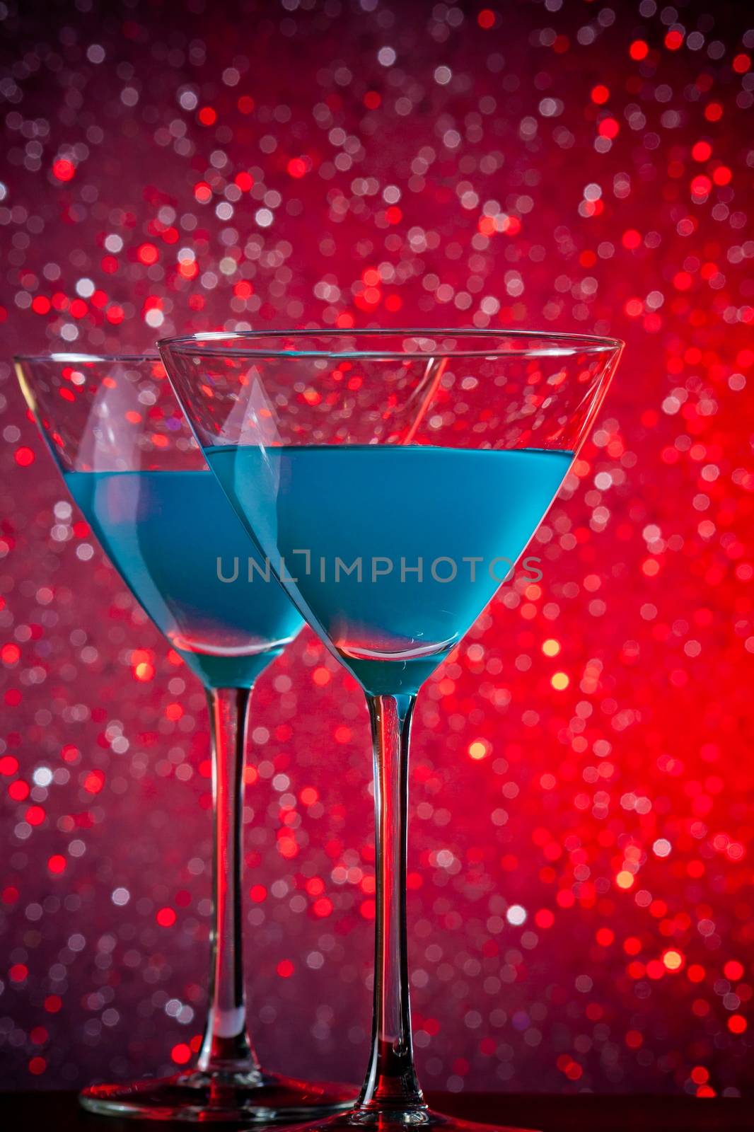 a pair of glasses of blue cocktail on red tint light bokeh background