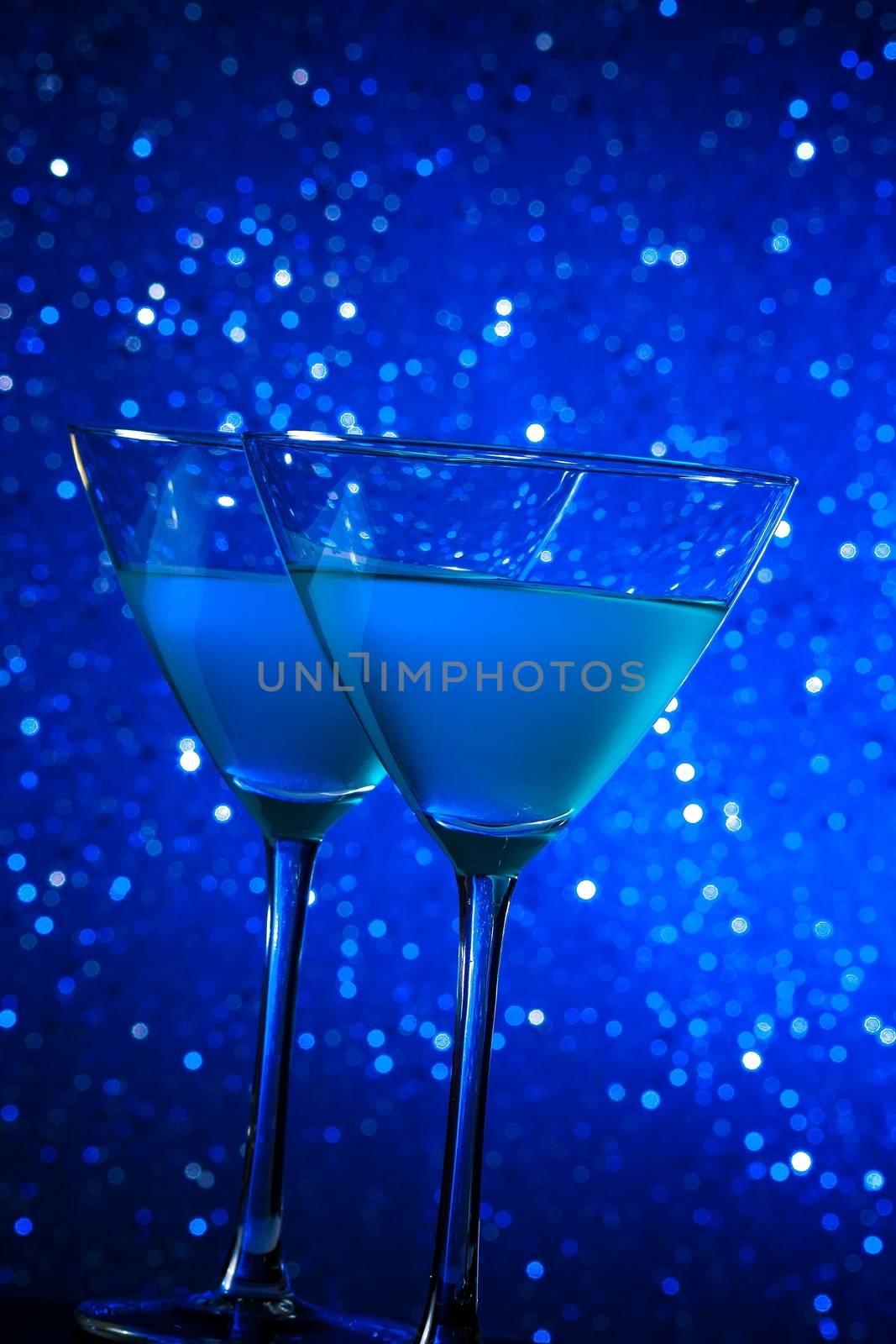 two glasses of blue cocktail on dark blue tint light bokeh background