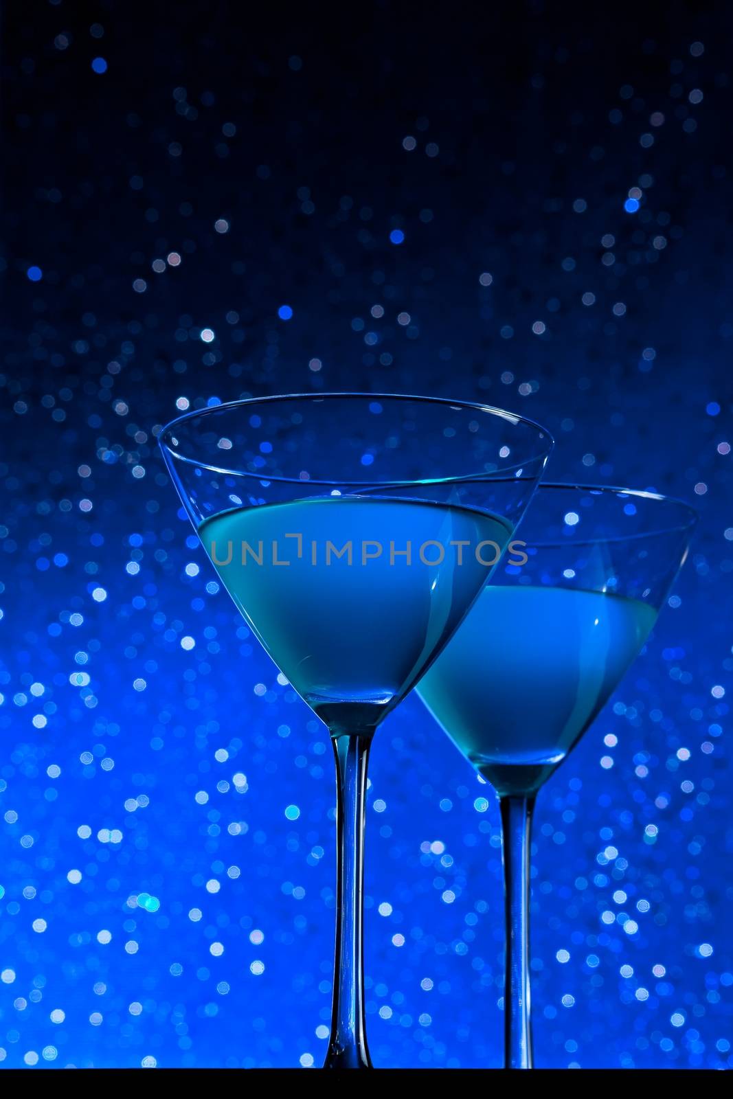 a pair of glasses of blue cocktail on dark blue tint light bokeh background