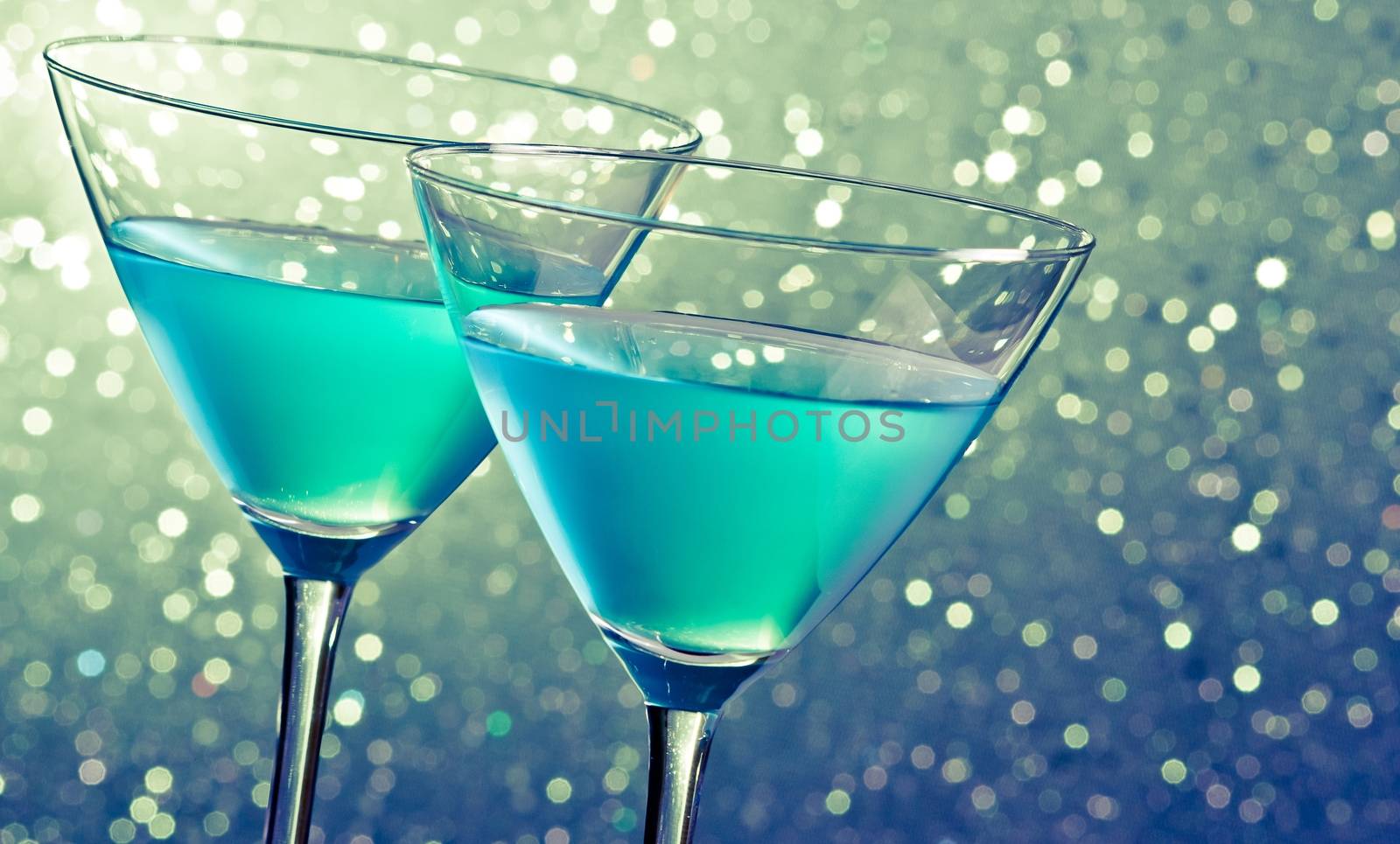 two glasses of blue cocktail on dark green tint light bokeh background on table
