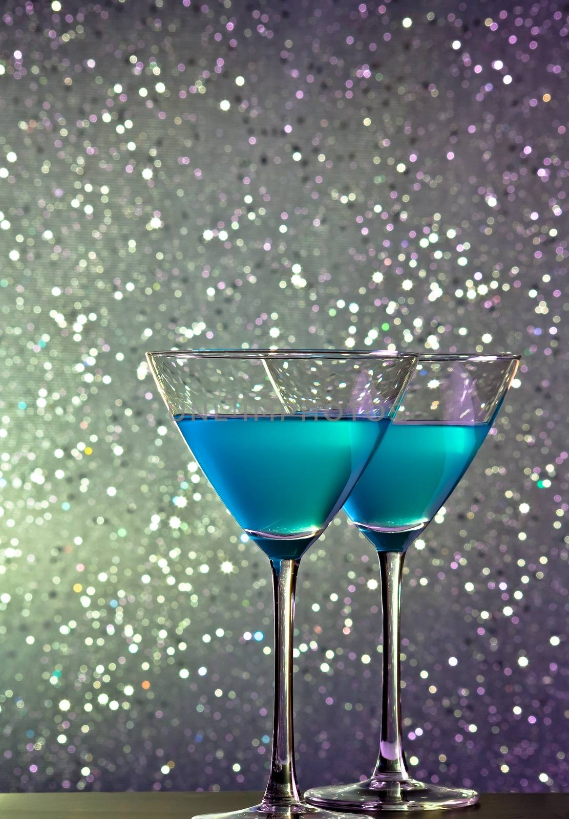 a pair of glasses of blue cocktail on silver tint light bokeh background on bar table