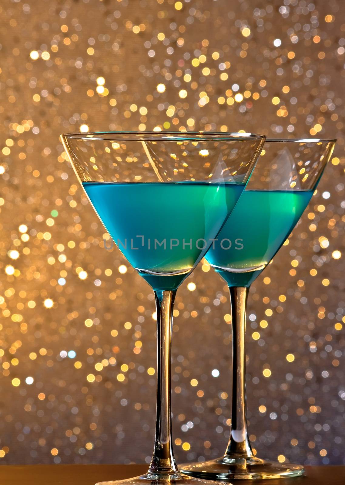 a pair of glasses of blue cocktail on golden tint light bokeh background on bar table