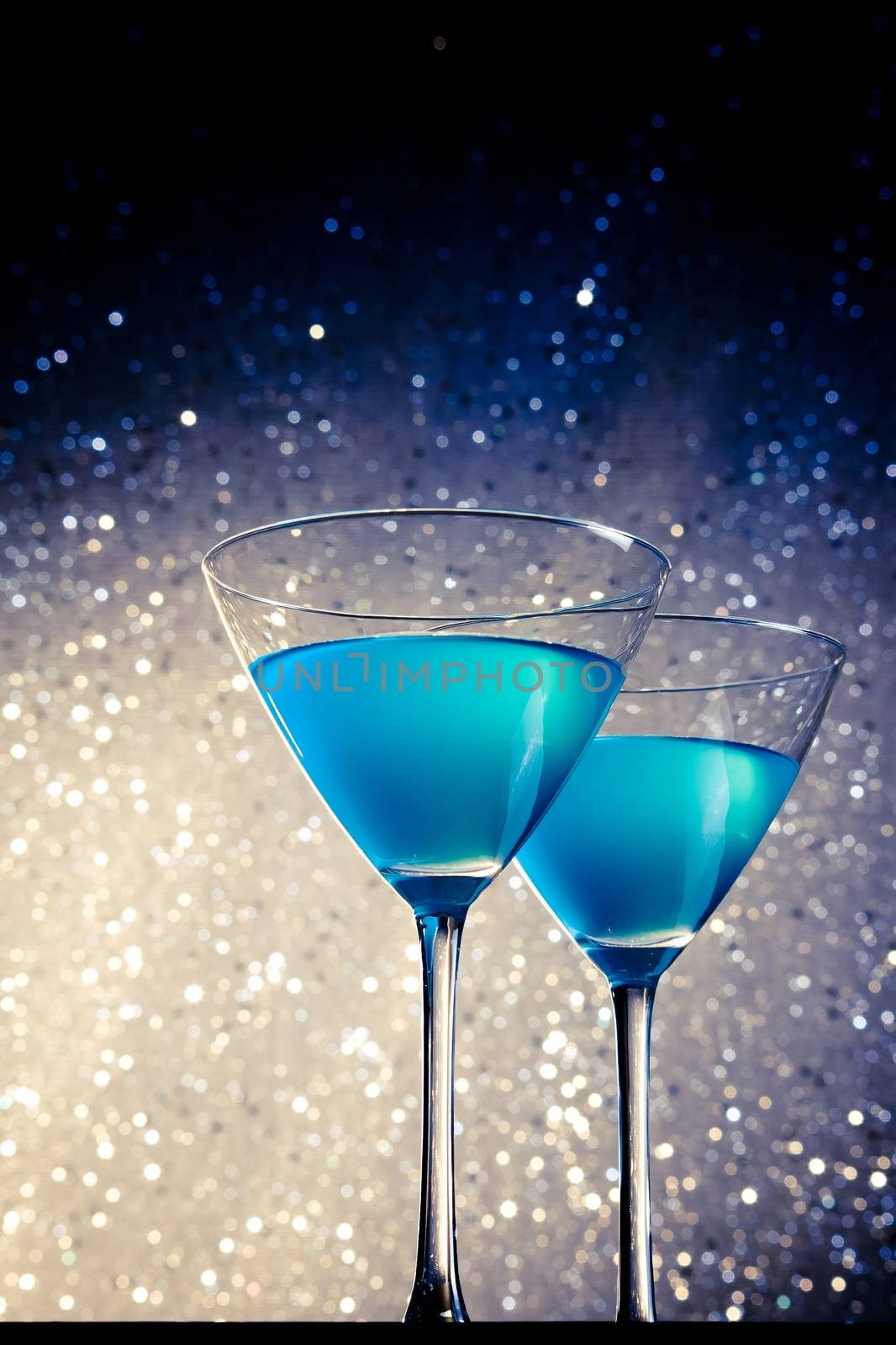 a pair of glasses of blue cocktail on white and dark tint light bokeh background
