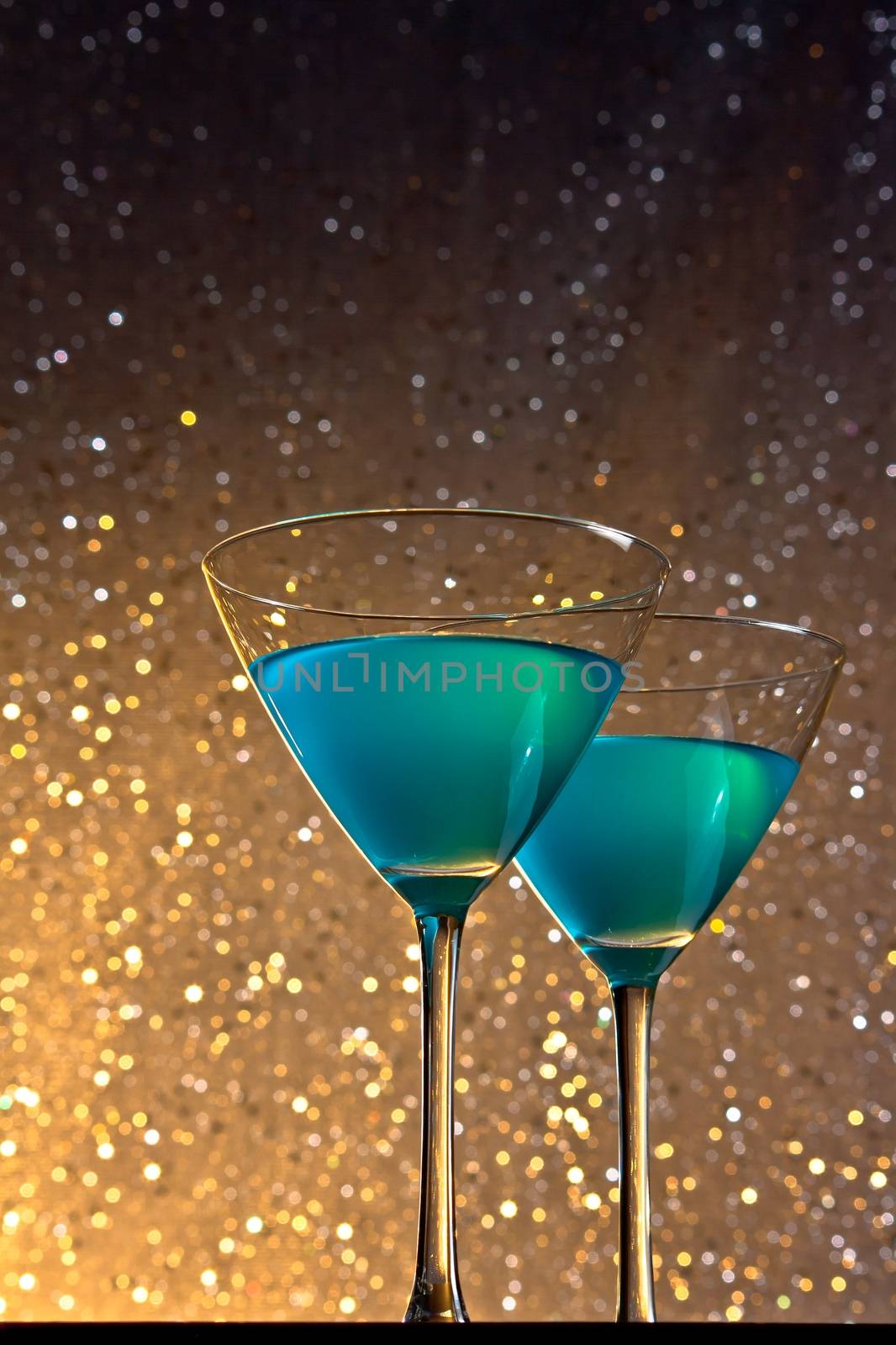 a pair of glasses of blue cocktail on golden dark tint light bokeh background