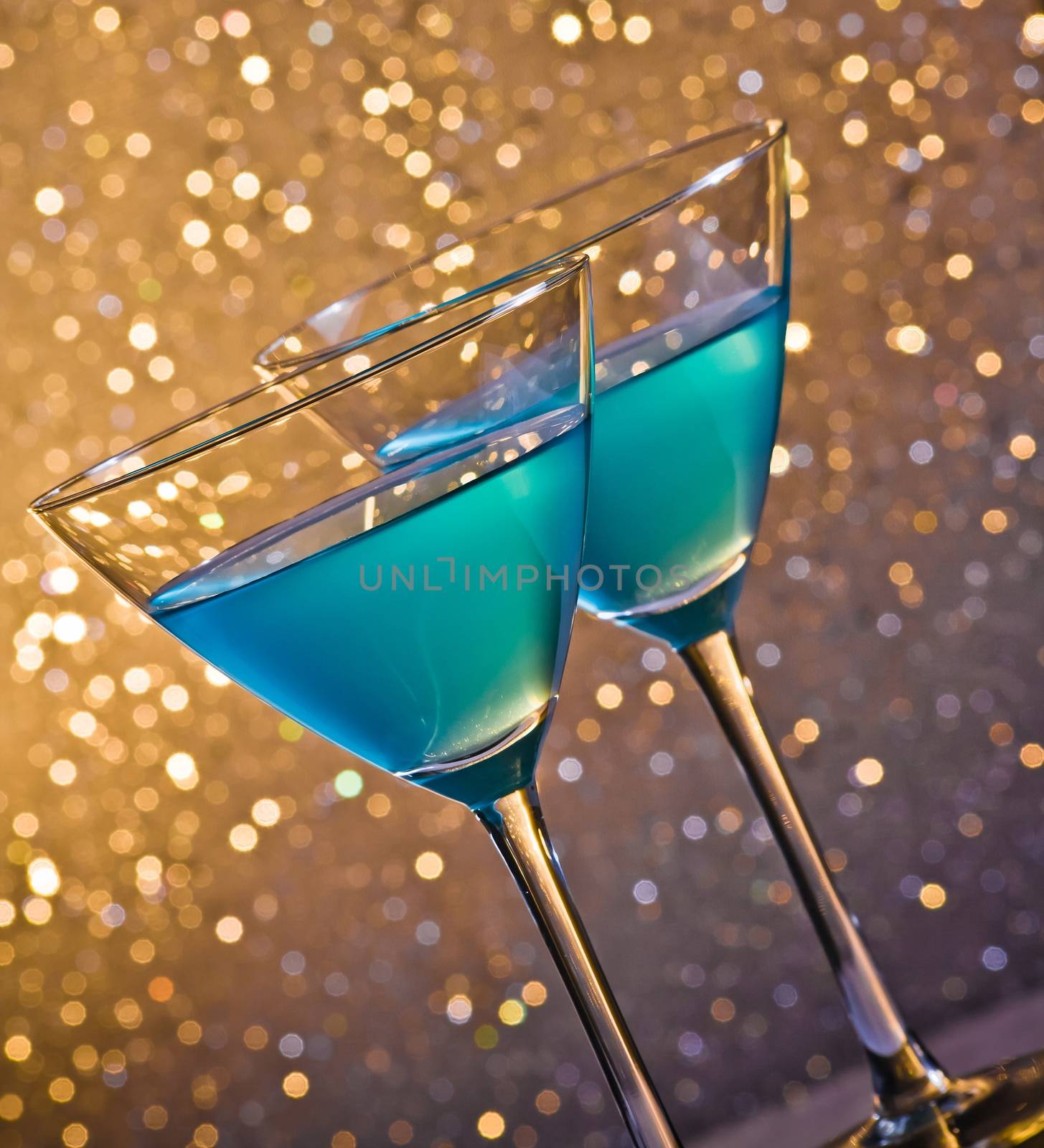 two glasses of blue cocktail on golden tint light bokeh background