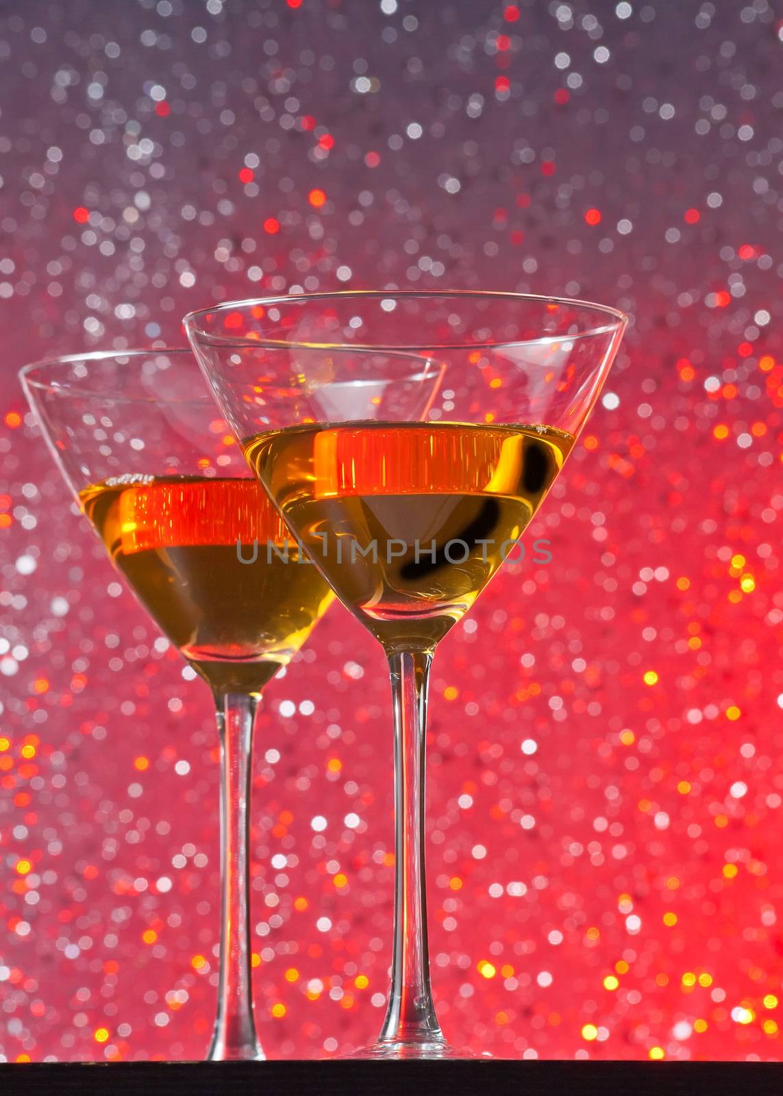 view from below of glasses of cocktail on red tint light bokeh background on bar table