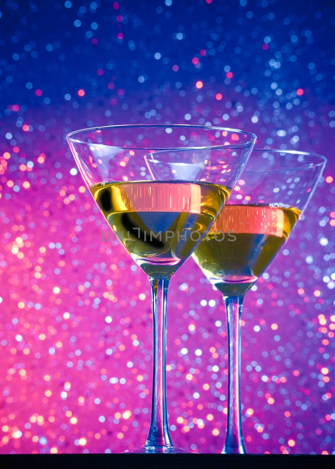 view from below of glasses of cocktail on blue and violet tint light bokeh background on bar table