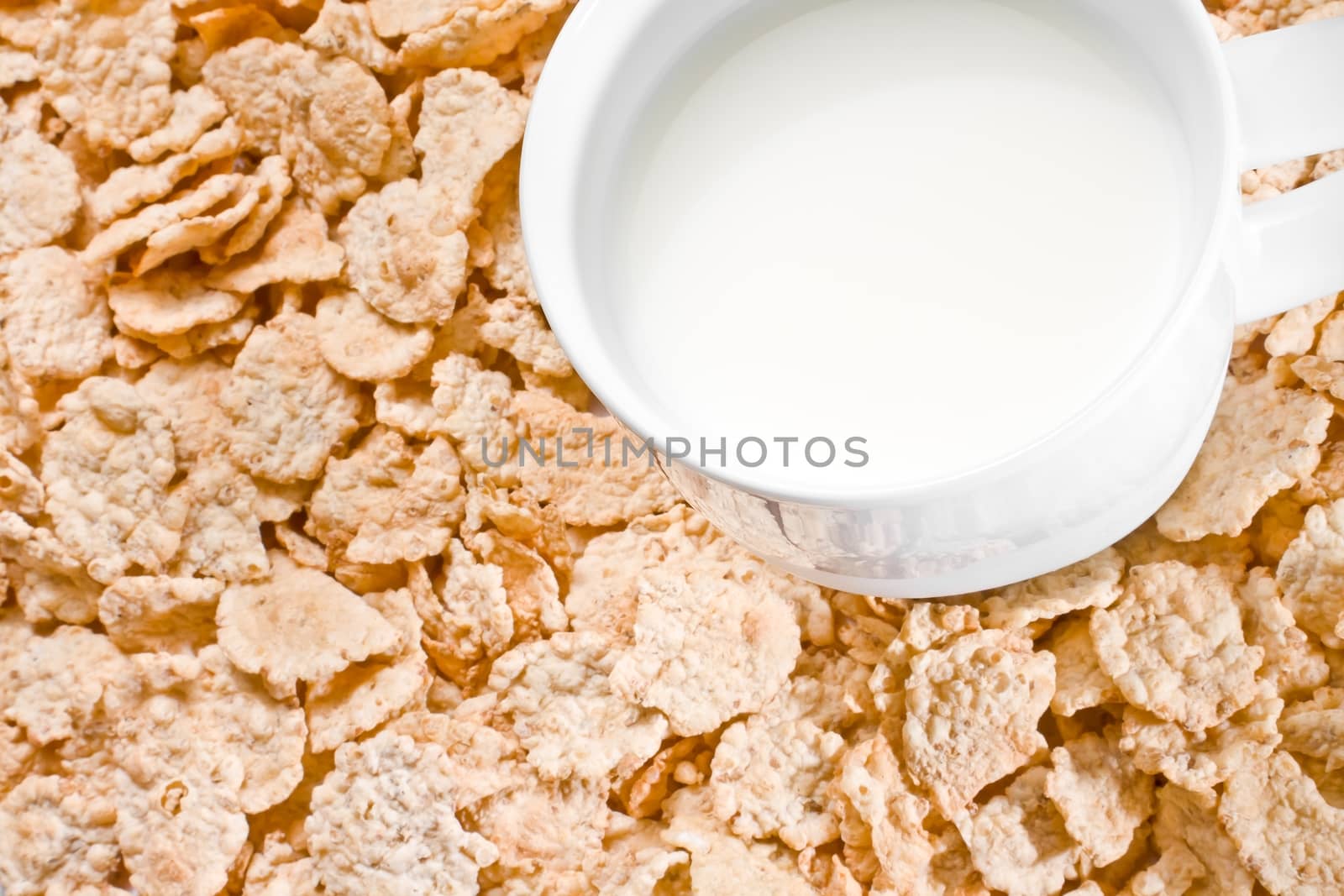detail of cup of milk on corn flakes background, breakfast concept