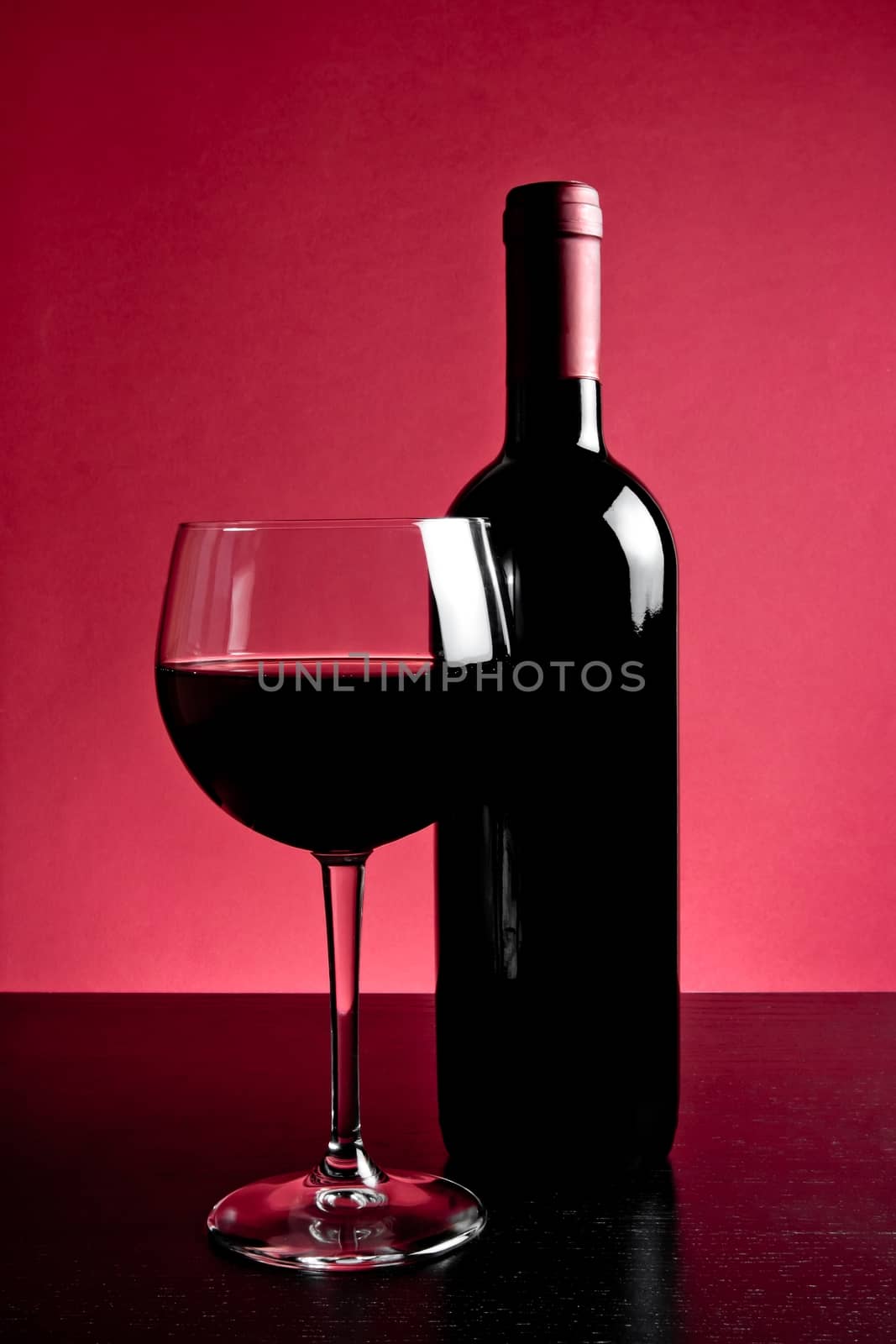 red wine glass near bottle on red background and wood table