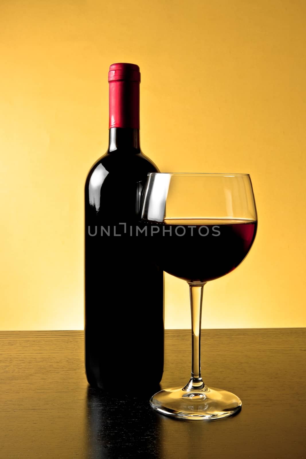 red wine glass near bottle on golden background and wood table
